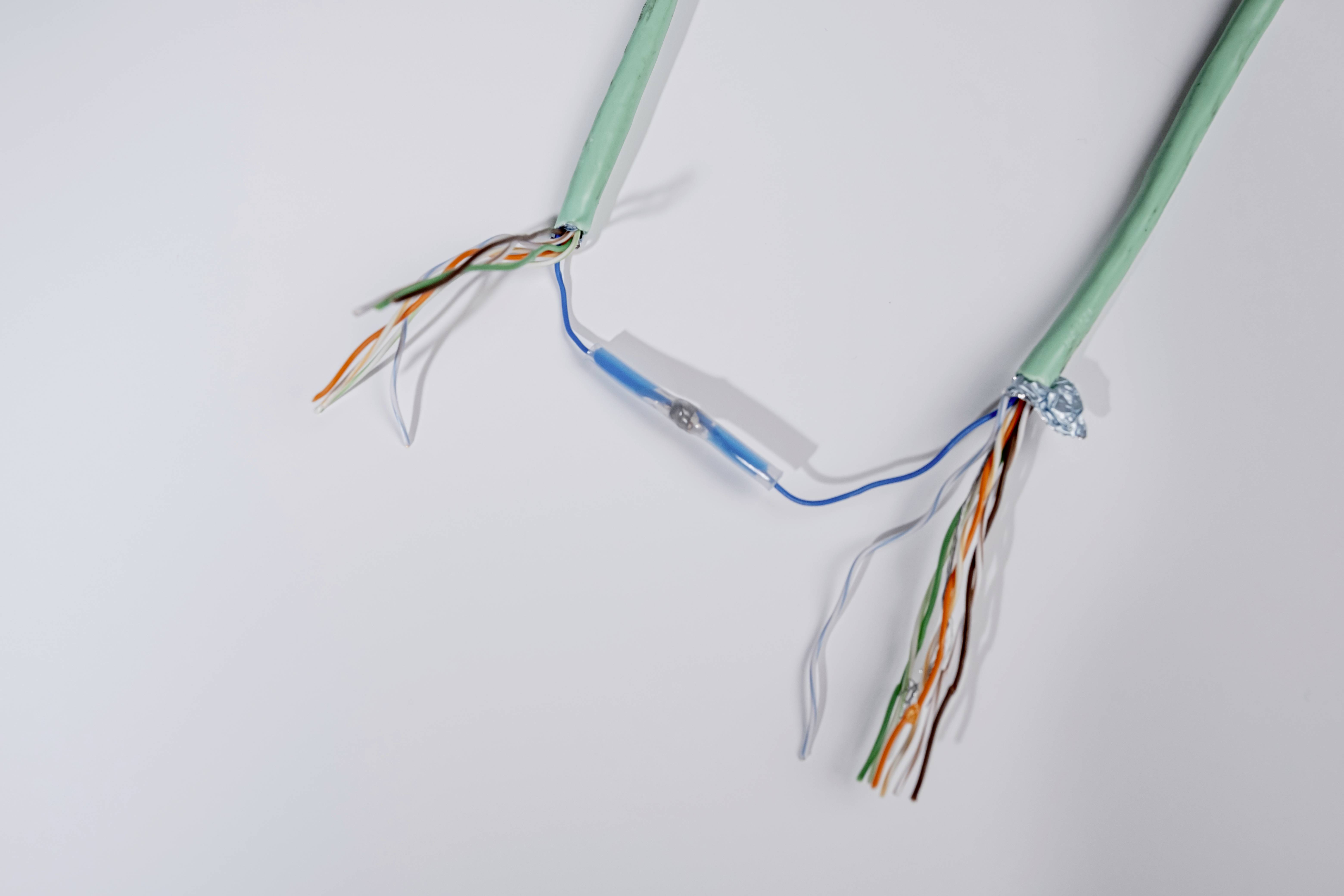 Ein grün ummanteltes Kabel mit freiliegenden, mehrfarbigen Drähten ist in der Mitte durchtrennt und mit einer blauen Verbindung fixiert.