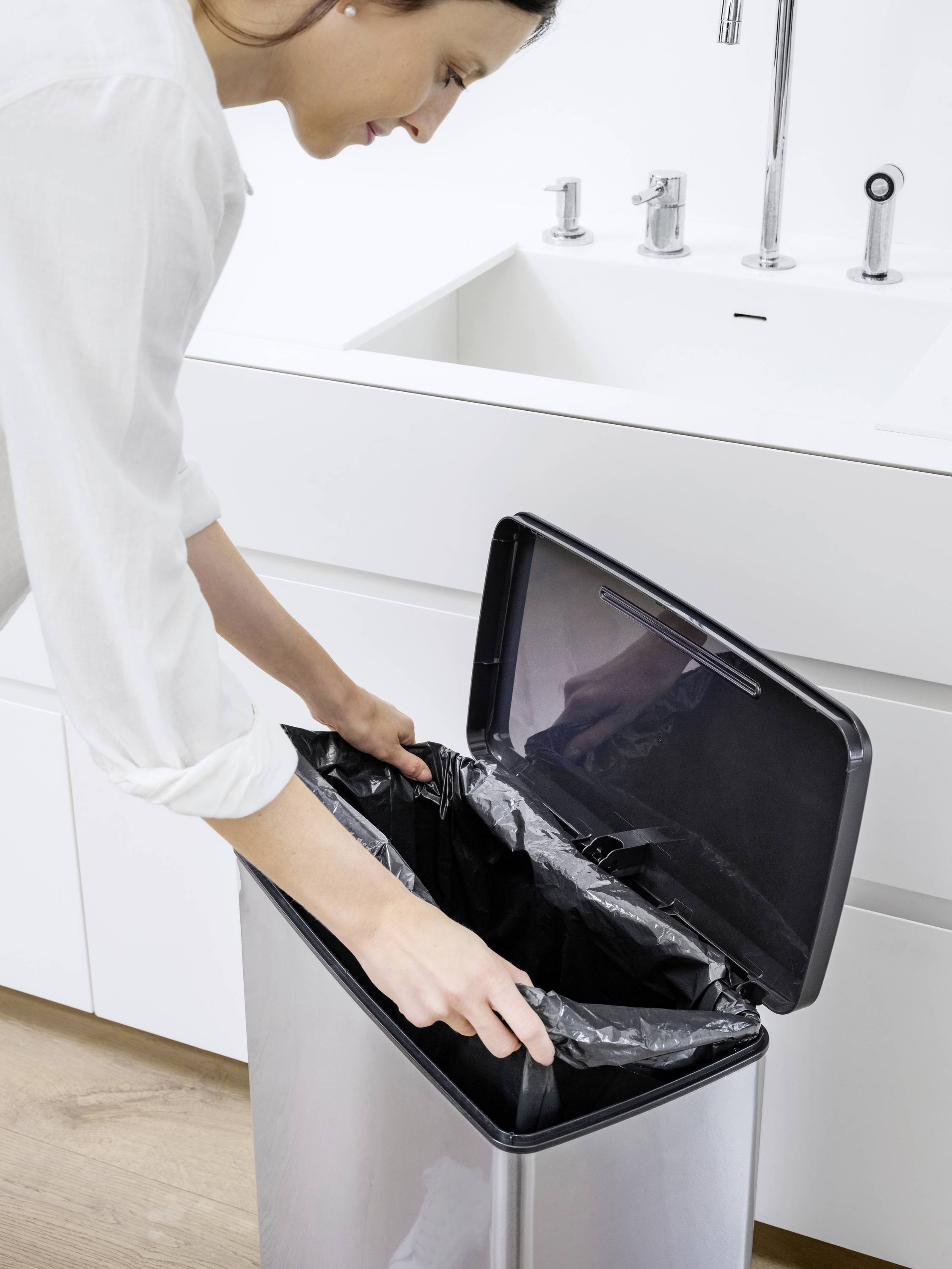 Eine Person wechselt einen Müllbeutel in einem Mülleimer in einer modernen Küche.