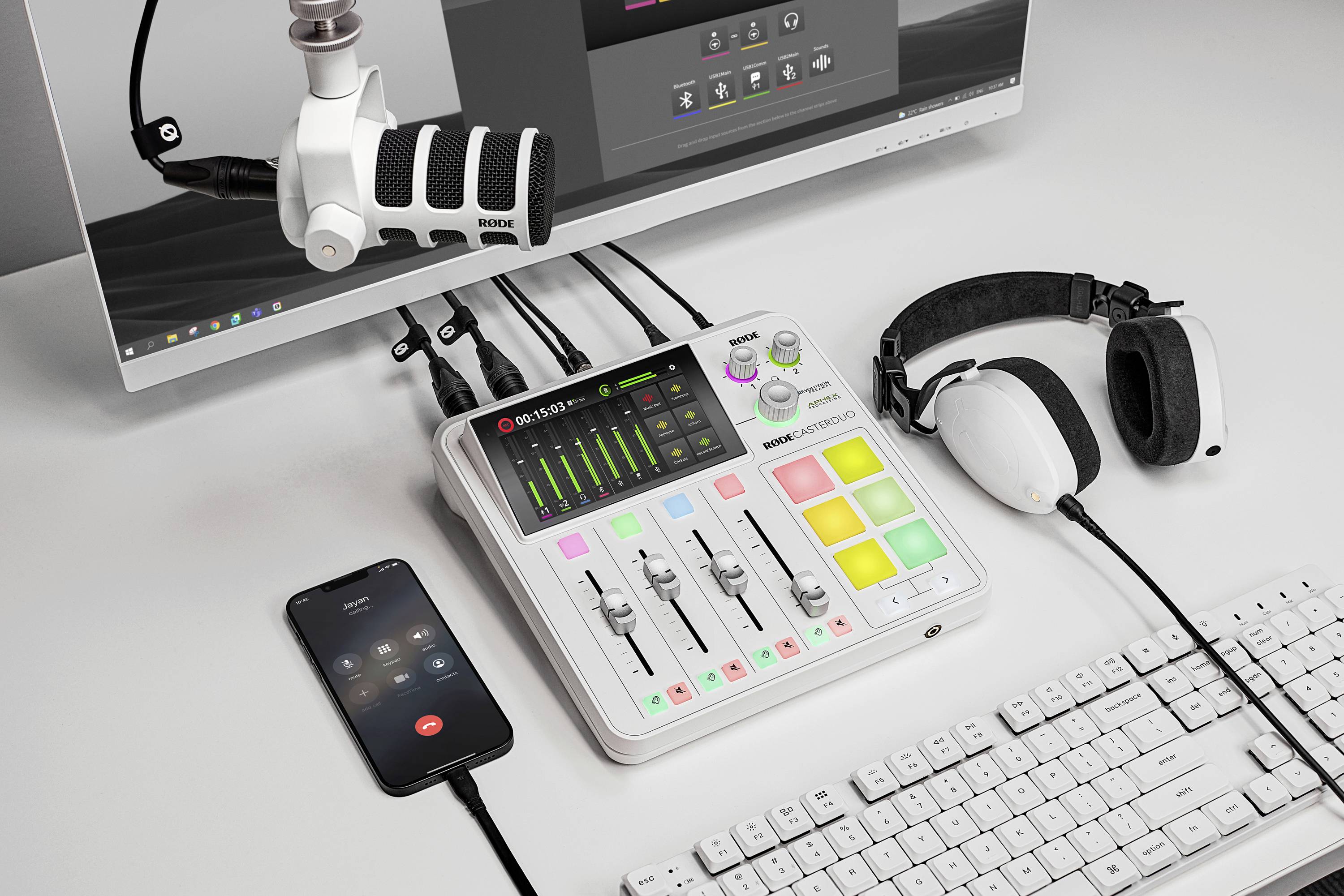 Ein Schreibtisch mit Audio-Setup: Mischpult mit Schiebereglern, beleuchteten Pads, Mikrofon, Kopfhörer und ein angeschlossenes Smartphone.