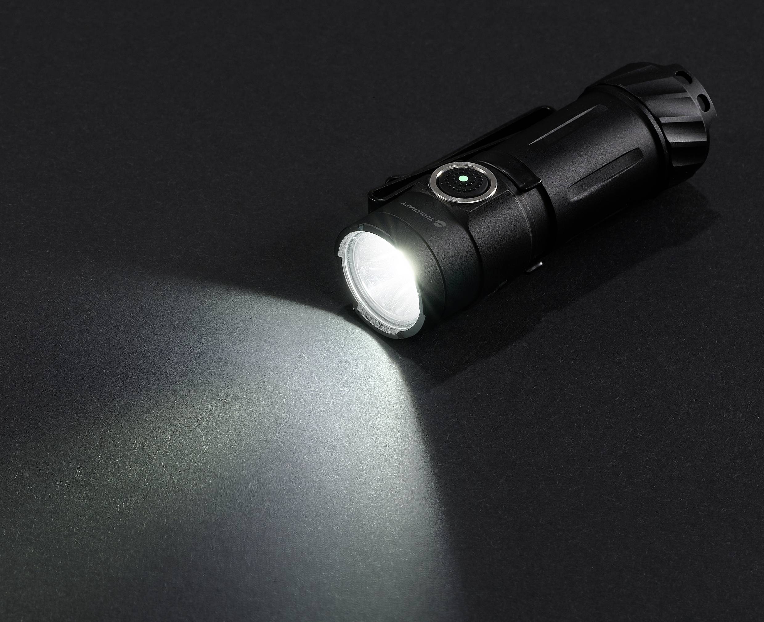 Taschenlampe leuchtet auf dunklem Hintergrund, Lichtstrahl schräg nach links unten gerichtet.