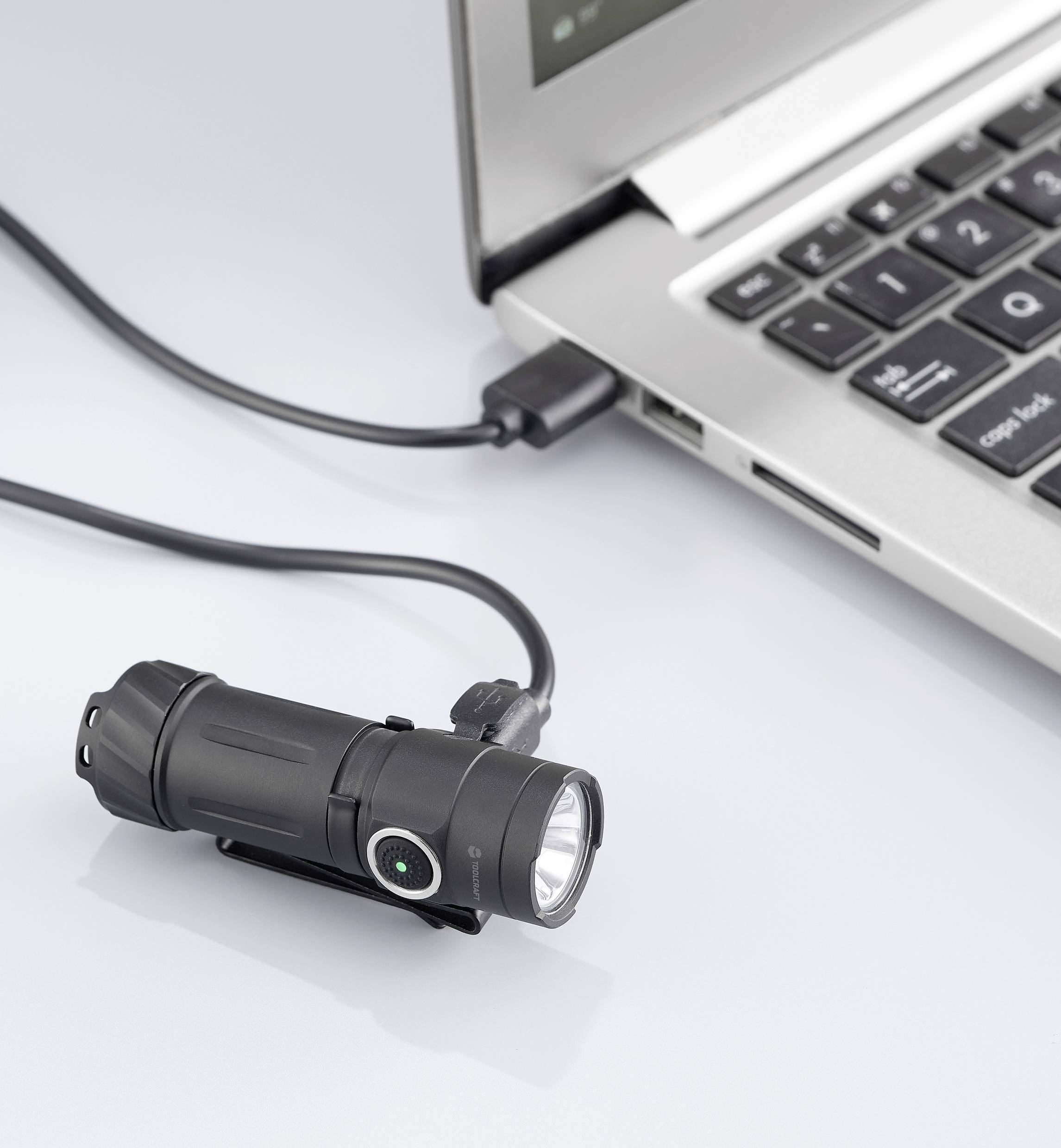 Eine Taschenlampe wird über ein USB-Kabel an einen Laptop auf einem weißen Tisch angeschlossen.