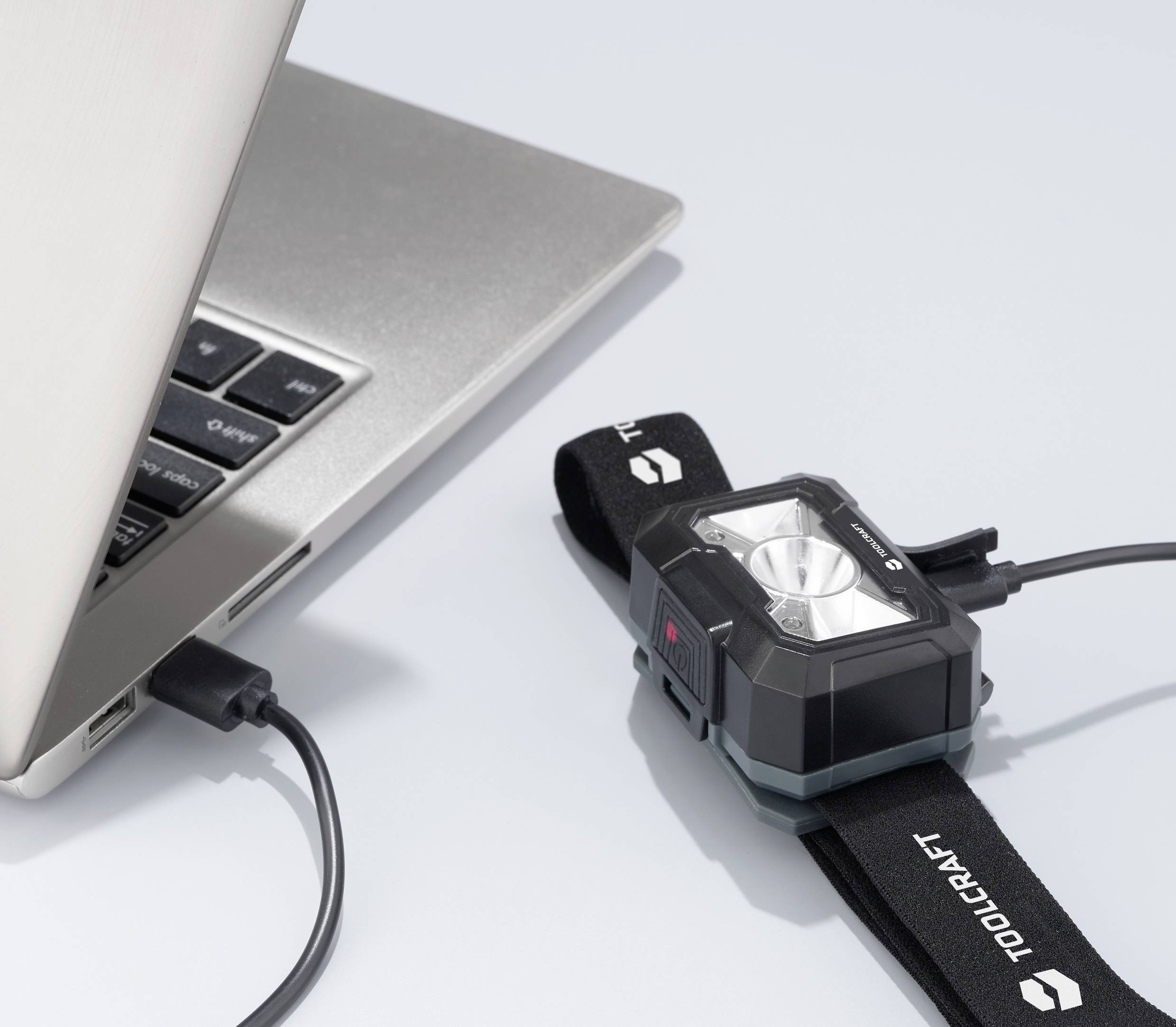 Eine Kamera ist mit einem Laptop über ein USB-Kabel verbunden, sie lädt oder synchronisiert Daten. Auf der Kamera steht 'TOOLCRAFT'.