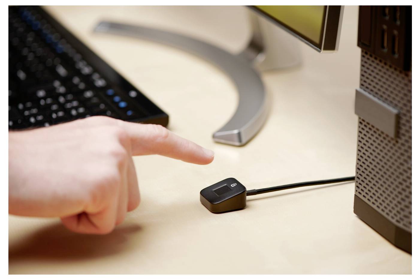 Jemand zeigt mit dem Finger auf einen USB-Computer-Schalter, der auf einem Tisch vor einem Monitor und einem Computer steht.