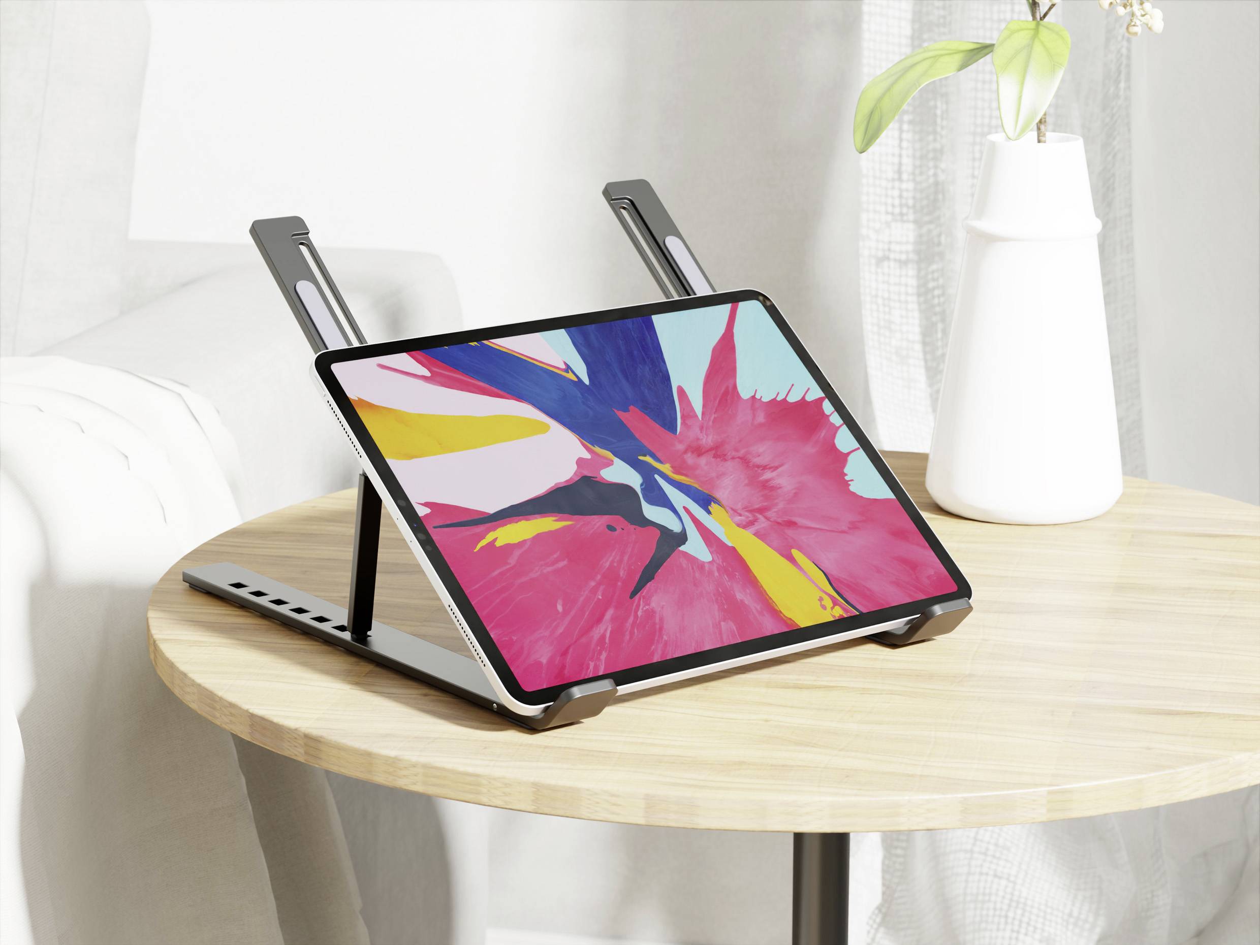 Ein Tablet, das abstrakte Kunst in leuchtenden Farben zeigt, steht auf einem Holztisch und wird von einem verstellbaren Ständer gestützt, neben einer weißen Vase mit einer Pflanze.