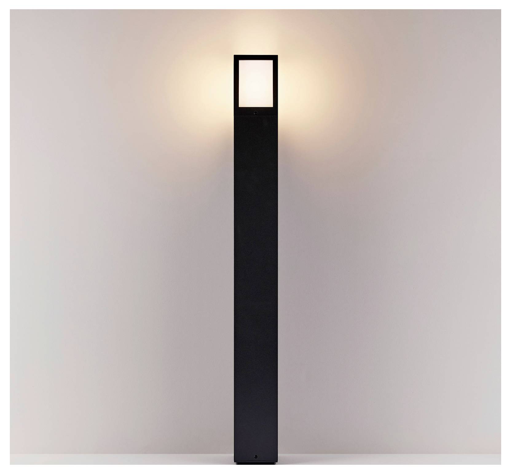 Minimalistische schwarze rechteckige Stehlampe, die sanft vor einer schlichten Wand leuchtet.