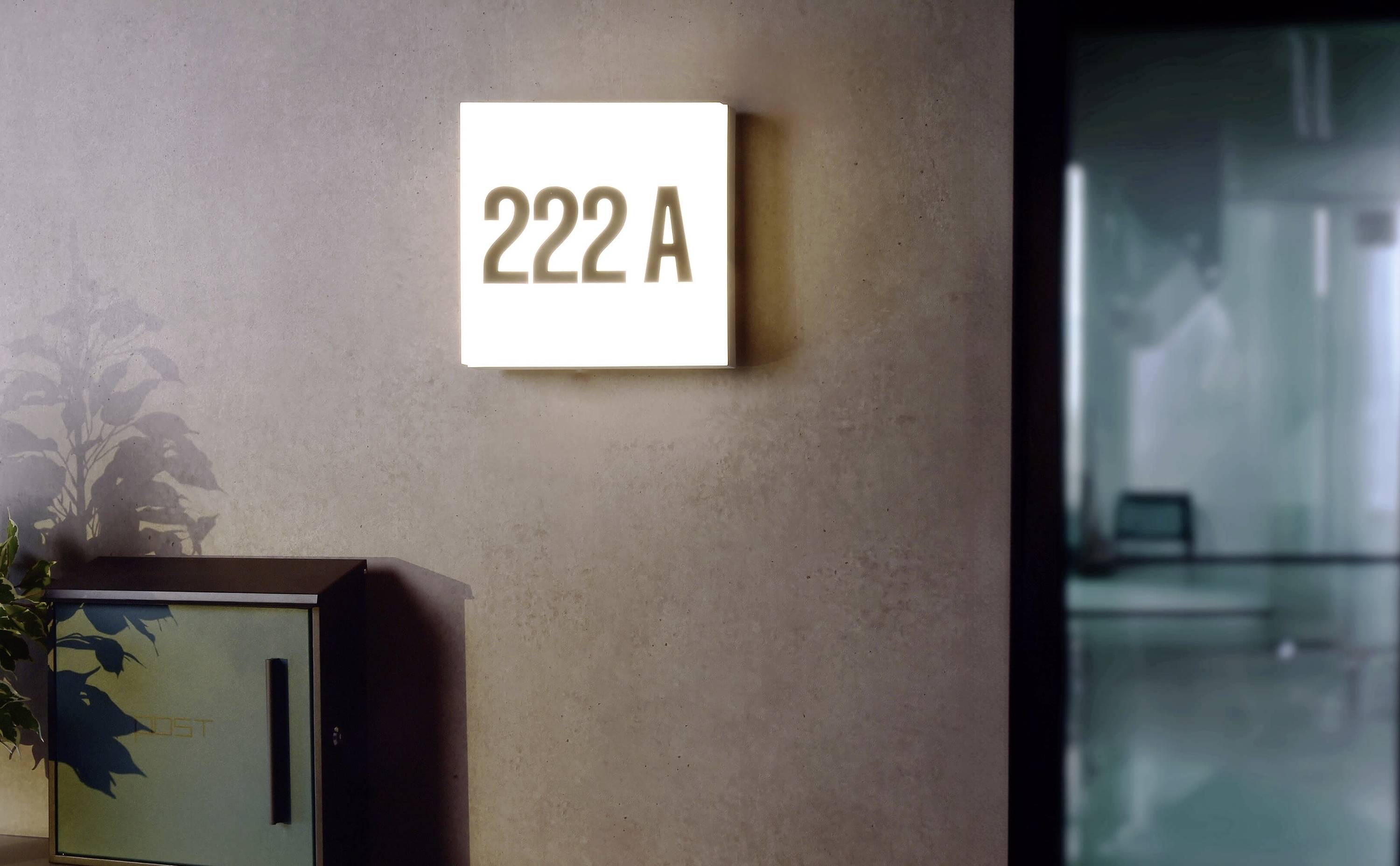 Eine leuchtende Türbeschilderung mit der Aufschrift '222 A' neben einer Tür, die zu einem modernen Büro führt.