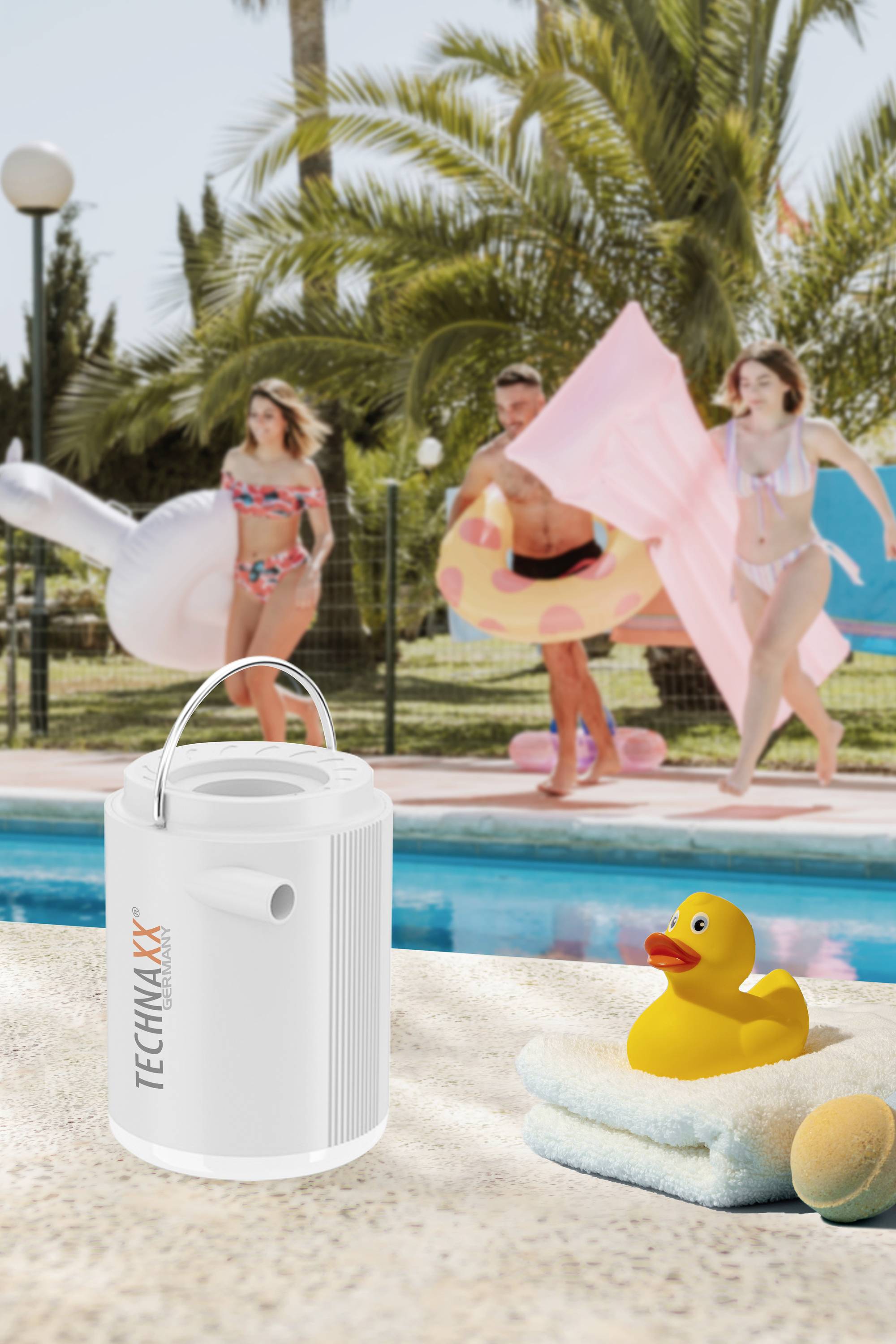 Ein weißer Lautsprecher und eine gelbe Badeente stehen am Pool. Im Hintergrund laufen drei Personen in Badebekleidung mit aufblasbaren Spielsachen.