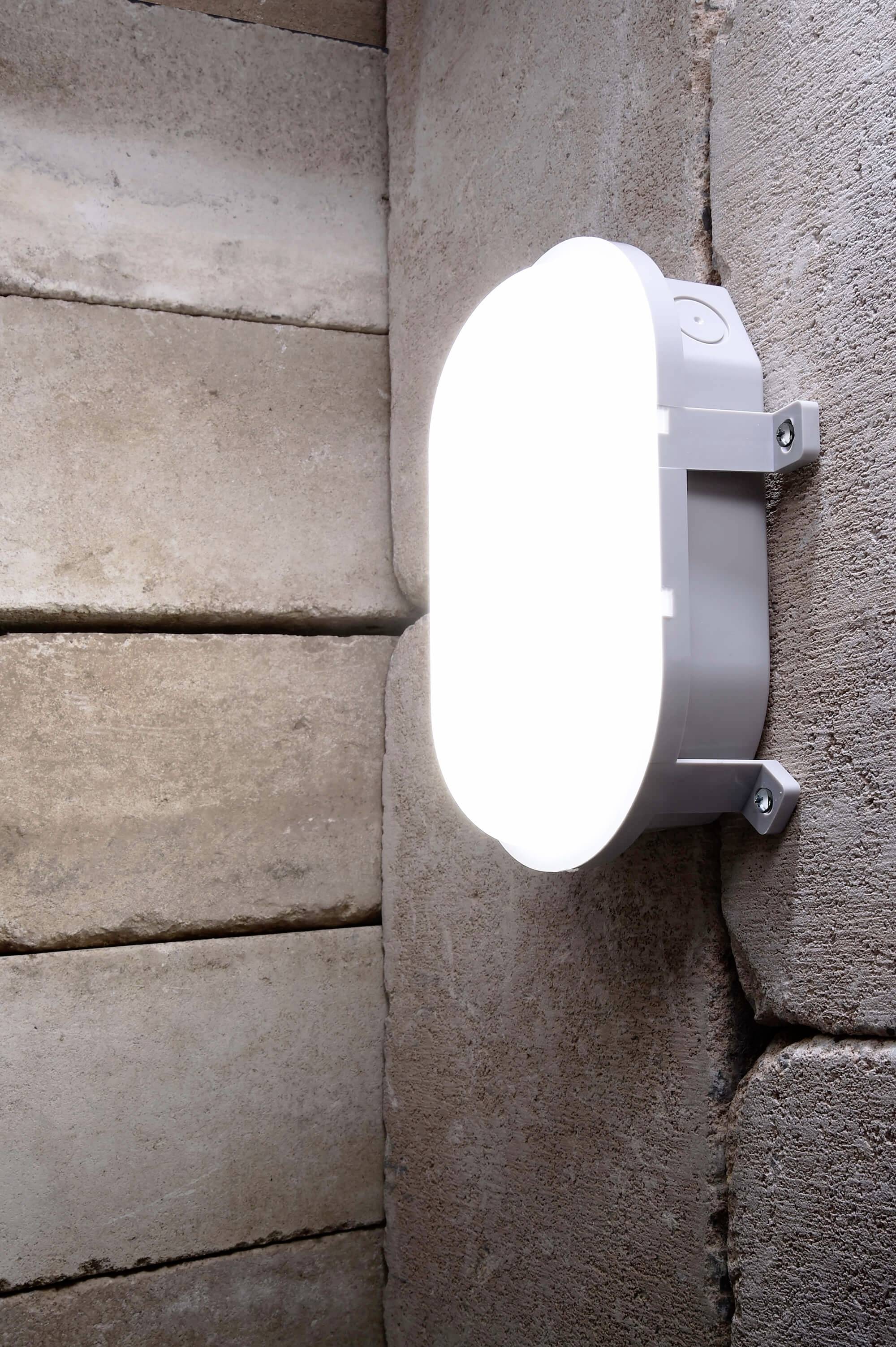 Eine helle Wandleuchte leuchtet an einer Wand aus rechteckigen Steinplatten und sorgt für klares Licht in einem rustikalen Raum.