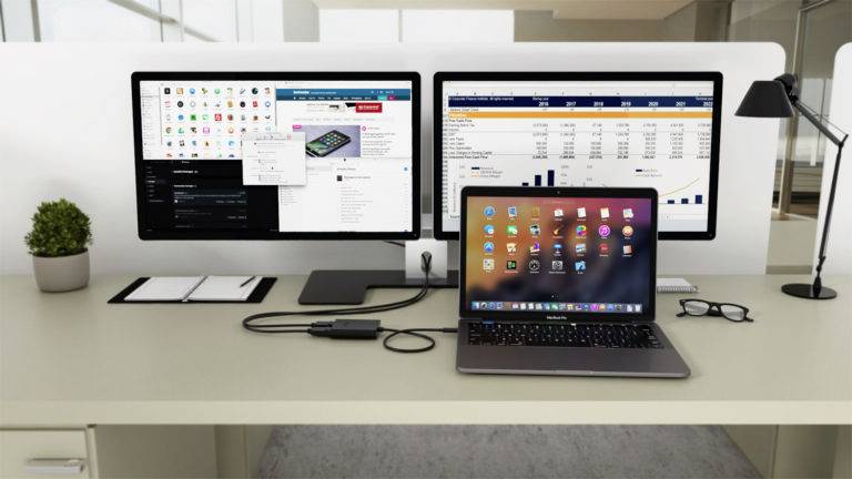 Ein moderner Schreibtisch mit zwei Monitoren, die Anwendungen und Tabellen zeigen, und einem Laptop, der mehrere Apps auf dem Bildschirm hat.