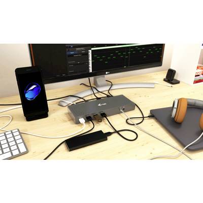 Ein Schreibtisch mit einem Monitor, der ein Musikprogramm zeigt, neben einem Computer, Smartphone, Audiokopfhörer und einer Dockingstation.