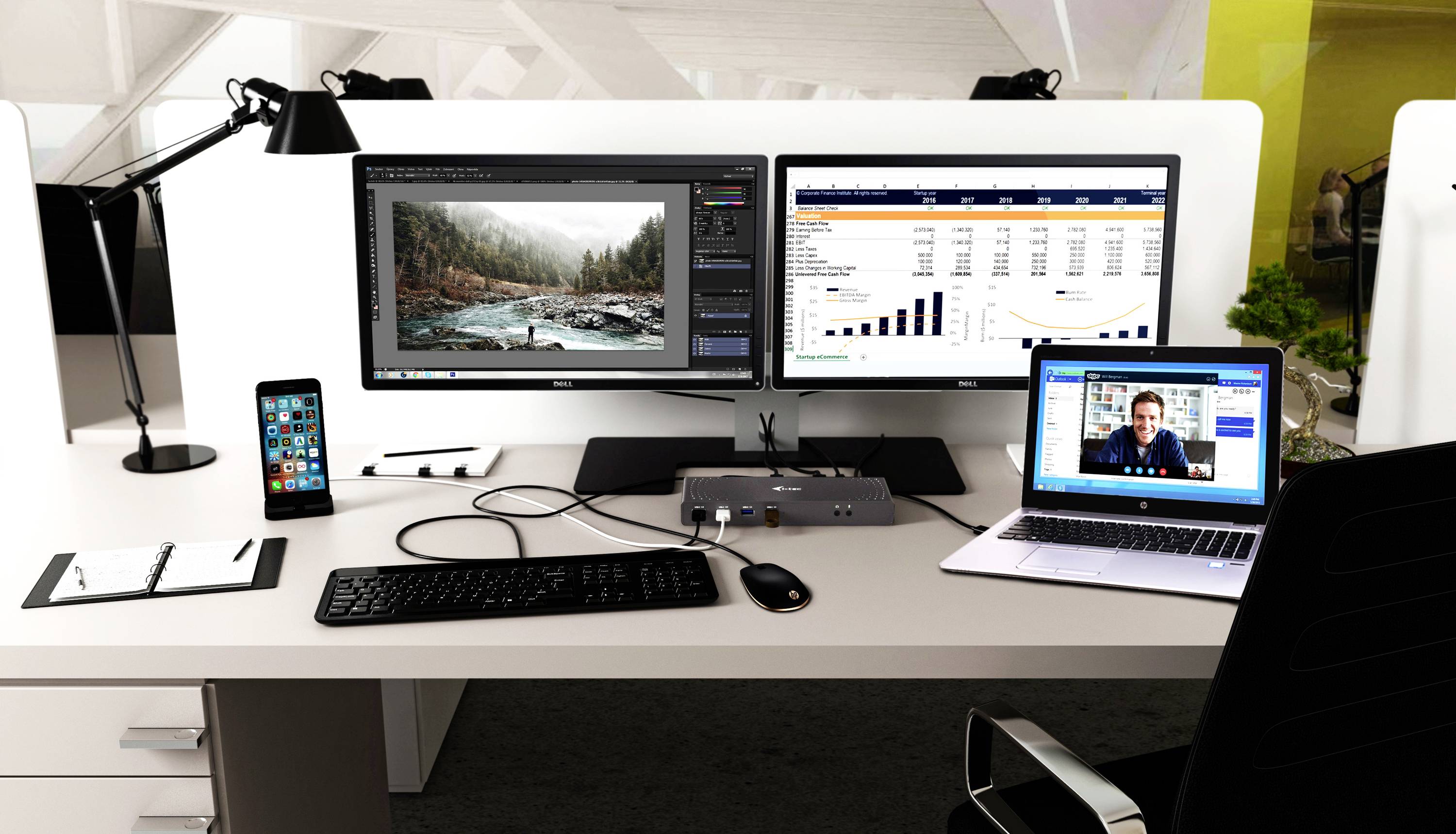 Ein Büroarbeitsplatz mit zwei Monitoren zeigt Bildbearbeitungssoftware und ein Tabellenkalkulationsprogramm. Ein Laptop zeigt ein Videogespräch.