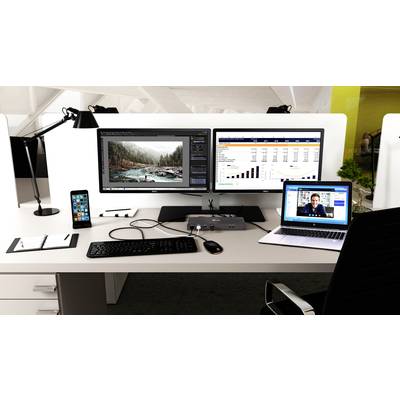 Ein Büroarbeitsplatz mit zwei Monitoren zeigt Bildbearbeitungssoftware und ein Tabellenkalkulationsprogramm. Ein Laptop zeigt ein Videogespräch.