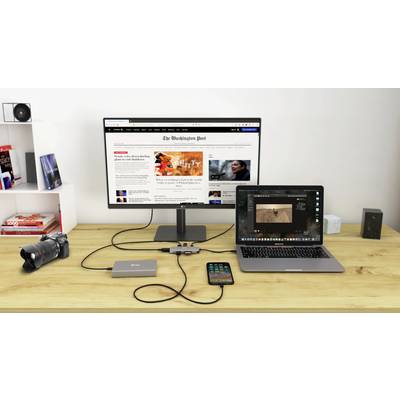 Ein Schreibtisch mit einem Monitor, der eine Nachrichtenseite anzeigt, ein Laptop mit Fotobearbeitungssoftware, eine Kamera und ein Smartphone.