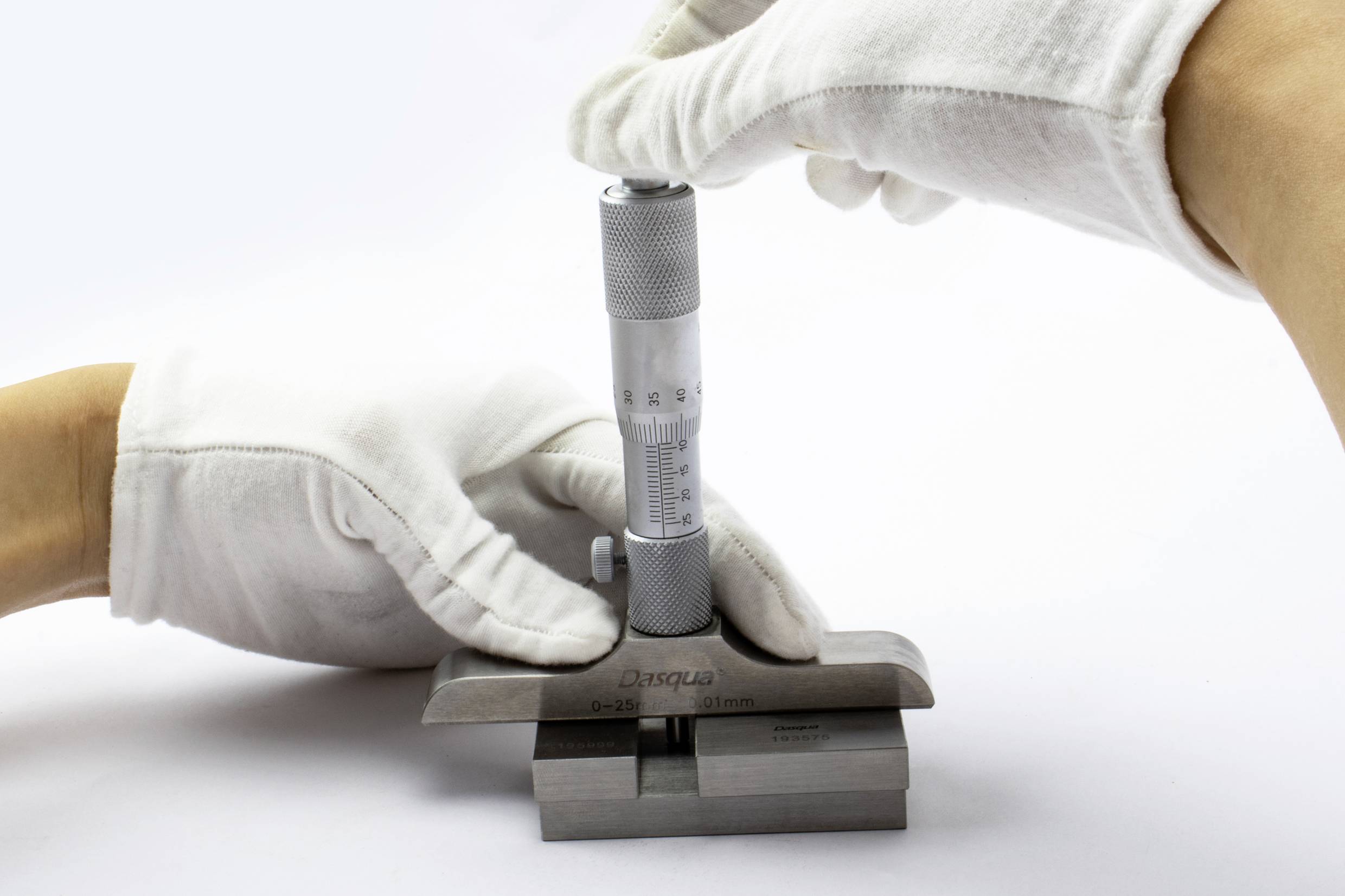 Eine Person in weißen Handschuhen misst mit einem Mikrometer die Dicke eines Metallblocks, um Präzision sicherzustellen.