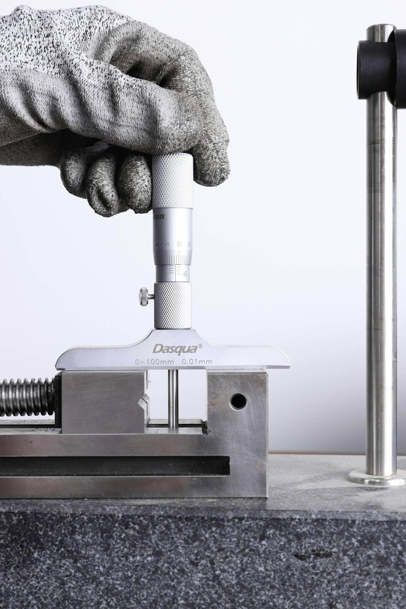 Eine behandschuhte Hand hält ein Tiefenmikrometer zur Messung der Tiefe eines Metallblocks, mit Präzisionsanzeige in Millimetern.