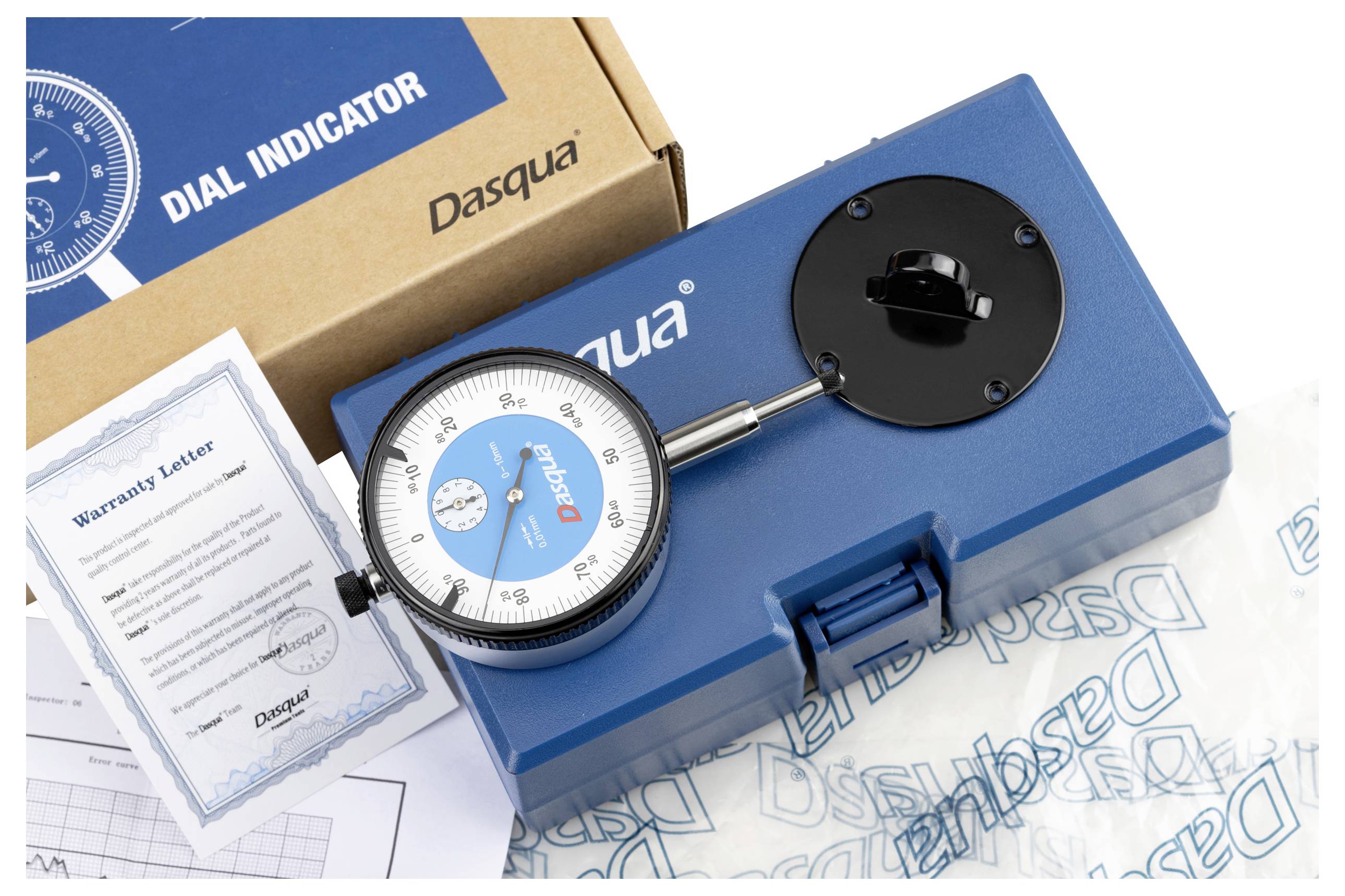 Ein blauer Messuhrkasten mit einem analogen Messgerät oben drauf. Daneben liegen ein Garantieschein und Verpackungsmaterial.