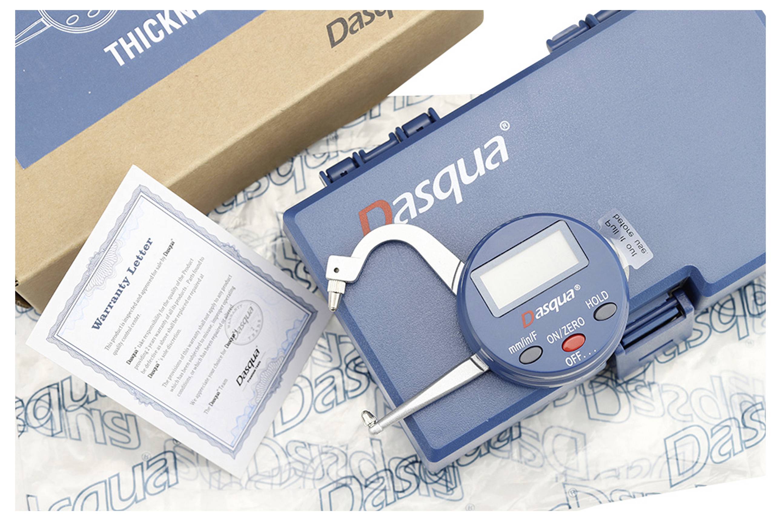 Digitaler Messschieber von Dasqua in blauem Gehäuse auf Verpackung und Garantieschein liegend.