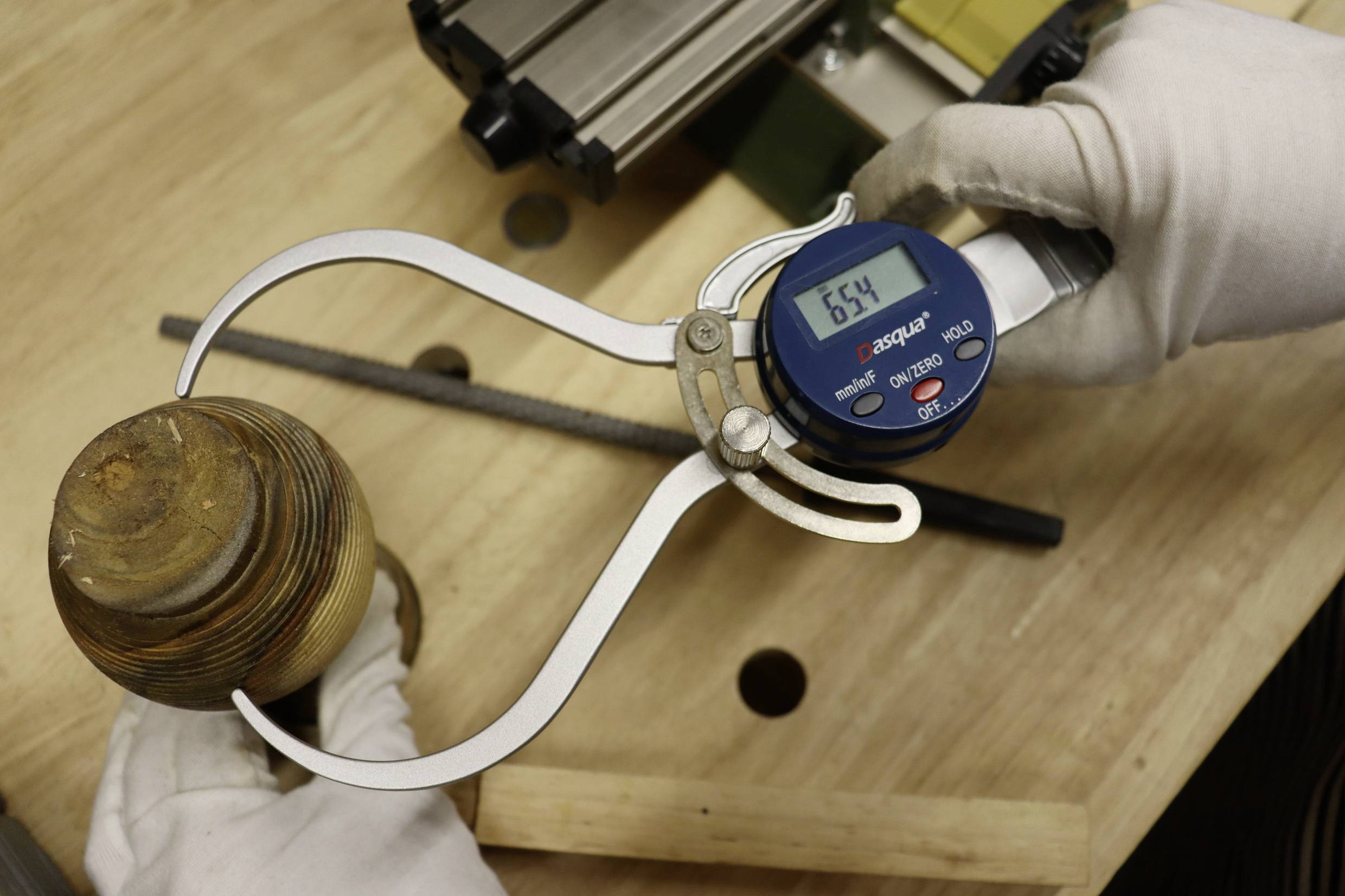 Hand hält digitale Messschieber an einem gedrechselten Holzobjekt auf einer Werkbank. Digitalanzeige zeigt 65,4 mm.