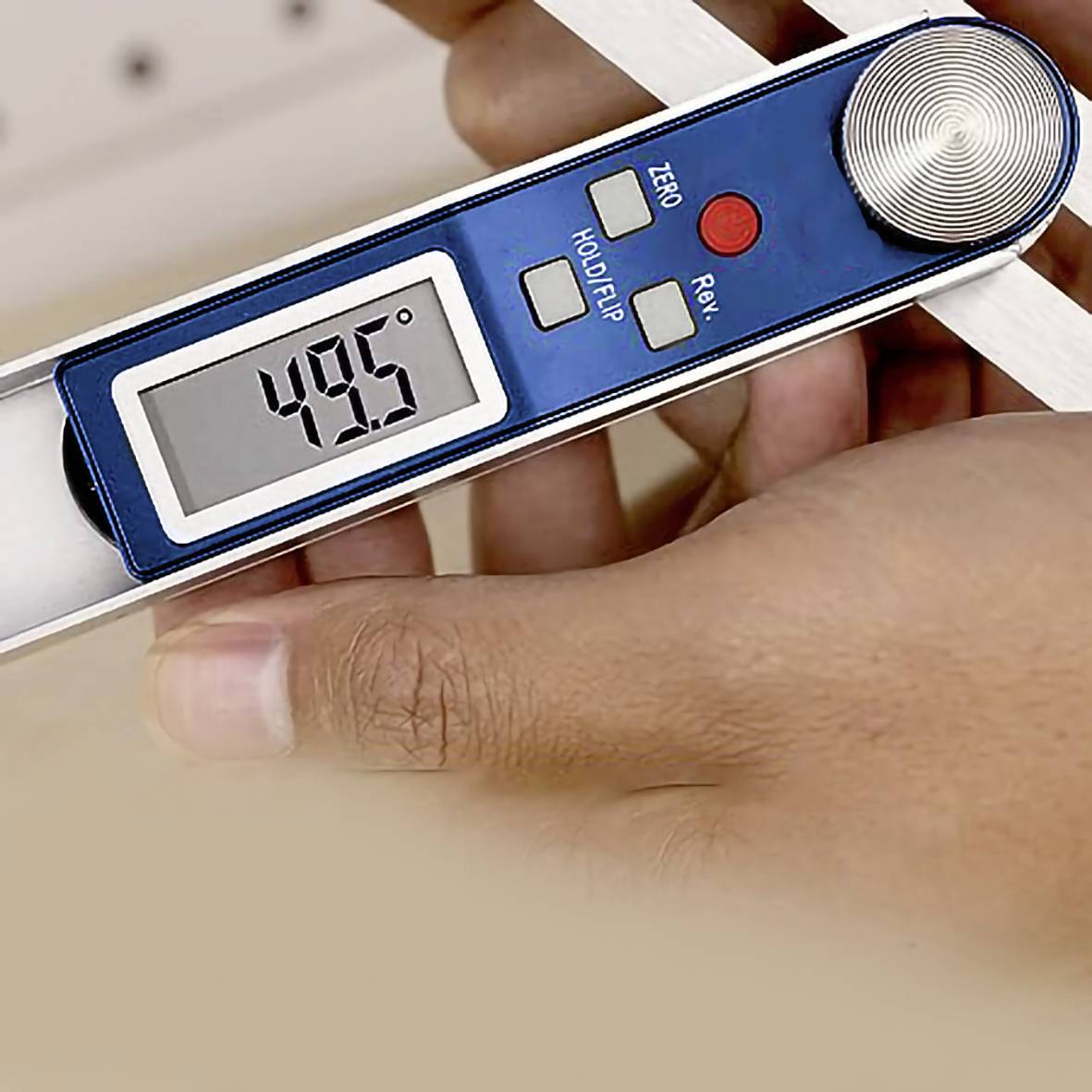 Eine Hand hält einen digitalen Winkelmesser, der einen Winkel von 49,5 Grad auf einem Display anzeigt. Geräteknöpfe sind sichtbar.