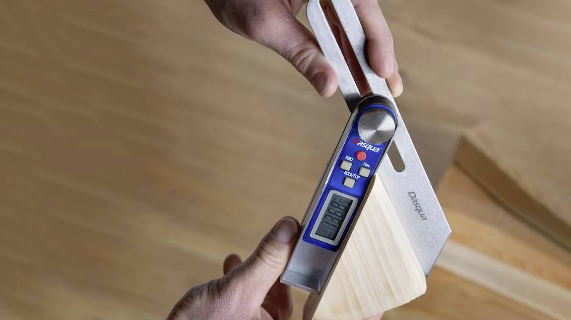 Eine Person misst mit einem digitalen Winkelmesser den Winkel eines Holzstücks. Der Bildschirm zeigt den genauen Messwert an.
