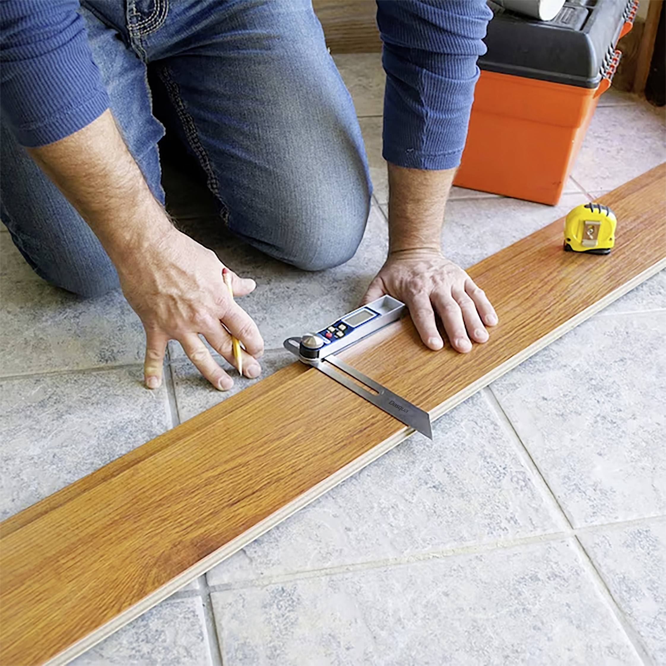 Person misst ein Holzbrett auf einem Fliesenboden mit einem Maßband und einem digitalen Winkelmesser.