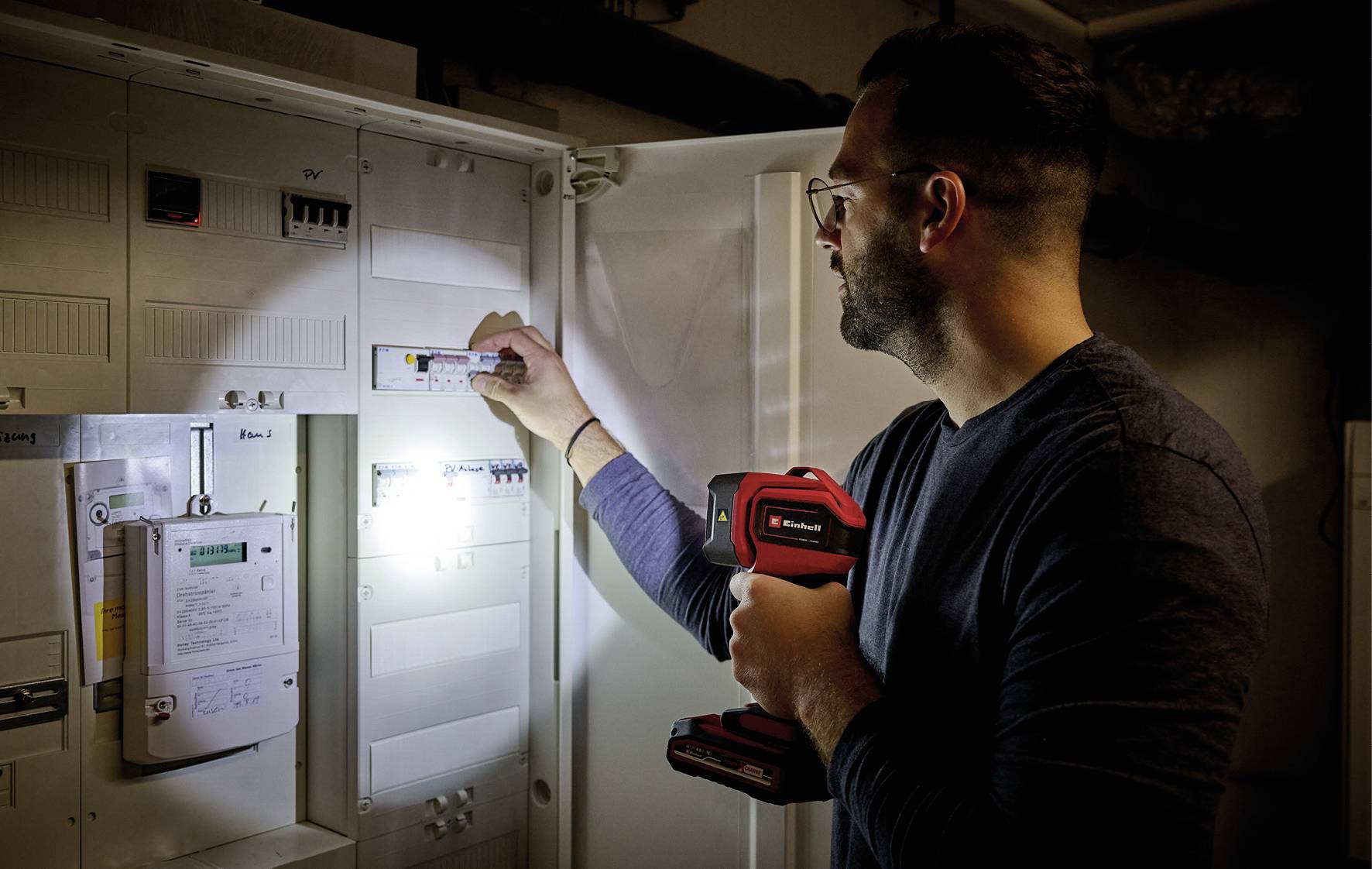Eine Person überprüft einen Sicherungskasten mit einer Taschenlampe in der Hand.
