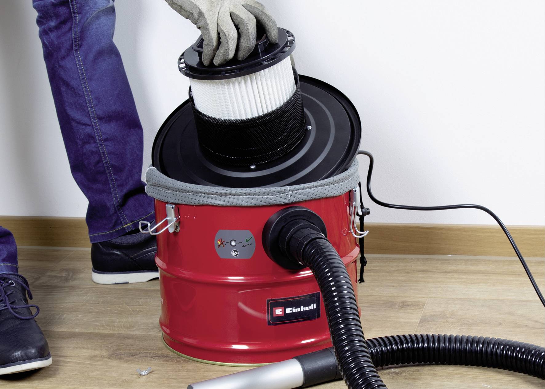 Eine Person wechselt den Filter eines roten Aschesaugers auf einem Holzboden.
