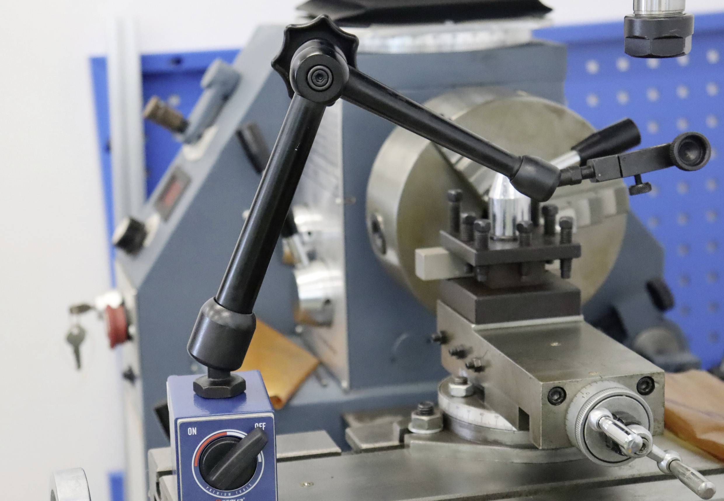 Eine Drehmaschine mit einem einstellbaren Haltearm und einem Bedienknopf. Im Hintergrund sind weitere Maschinenteile zu sehen.