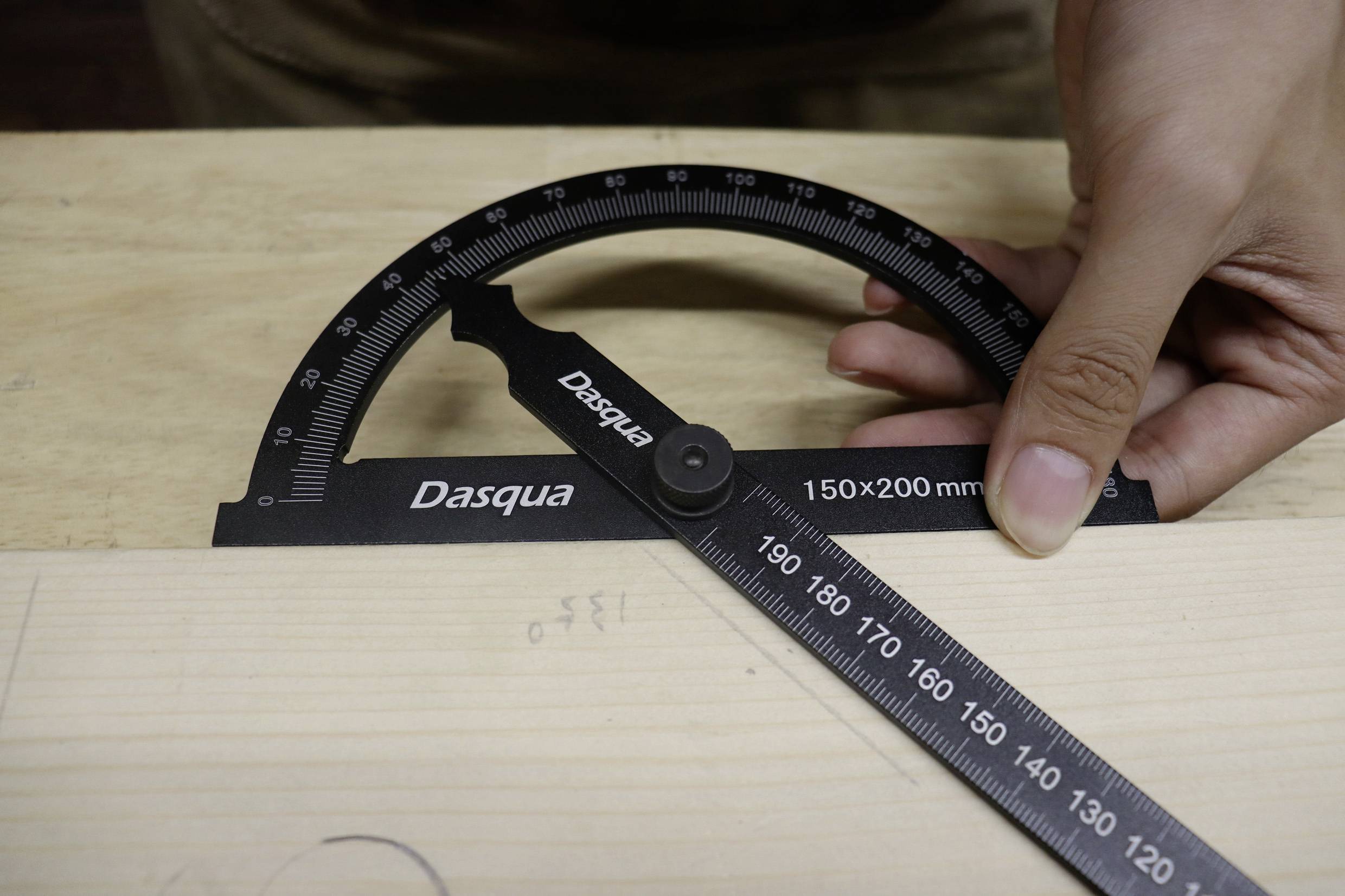 'Eine Hand hält einen Winkelmesser, der auf einem Holztisch positioniert ist, um den Winkel einer Kante zu messen.'
