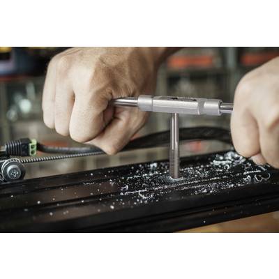 Zwei Hände schneiden mit einem Gewindebohrer ein neues Gewinde in ein Metallstück. Metallspäne sind zu sehen.