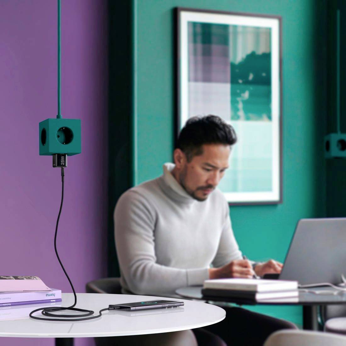 Ein Mann im Büro sitzt konzentriert am Schreibtisch, notiert in einem Notizbuch. Ein Laptop und Bücher befinden sich vor ihm.