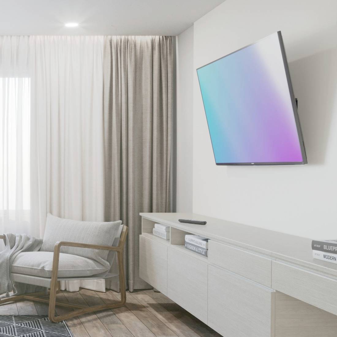 Ein moderner Wohnraum mit einem an der Wand montierten Flachbildfernseher, einem Sessel mit Kissen und einer hellen Gardine.