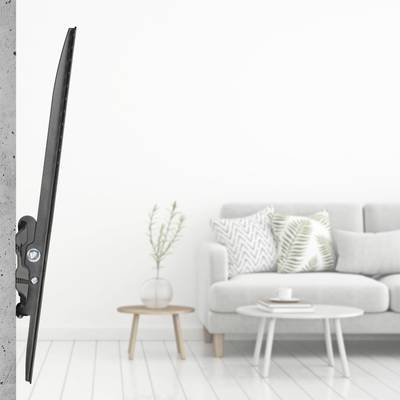Ein schlanker Fernseher ist an einer grauen Betonwand montiert. Im Hintergrund steht ein Sofa mit Kissen und ein kleiner Tisch mit Pflanzen.