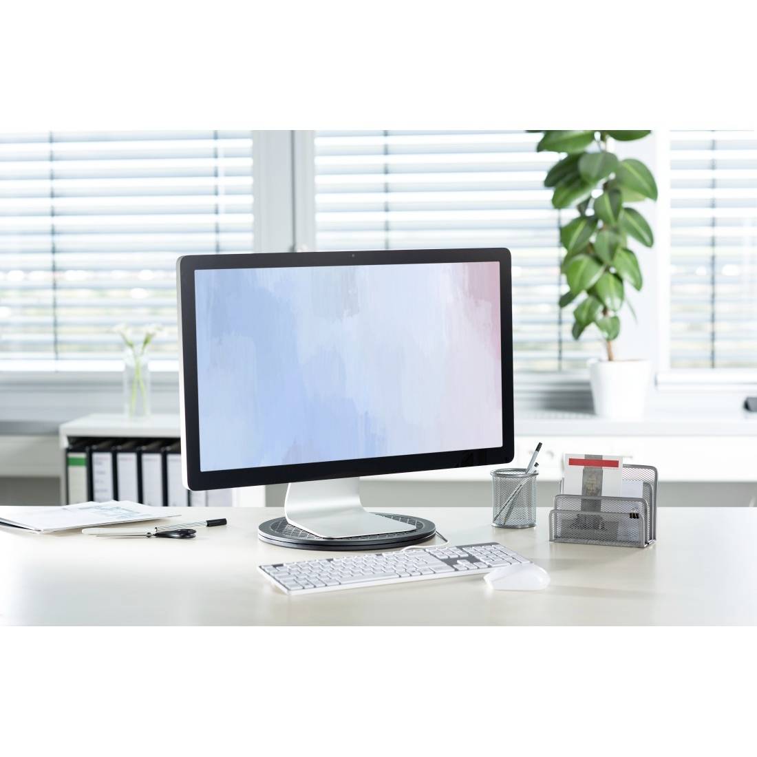 Ein moderner Computermonitor auf einem weißen Schreibtisch, umgeben von Büromaterialien und einer Topfpflanze im Hintergrund.