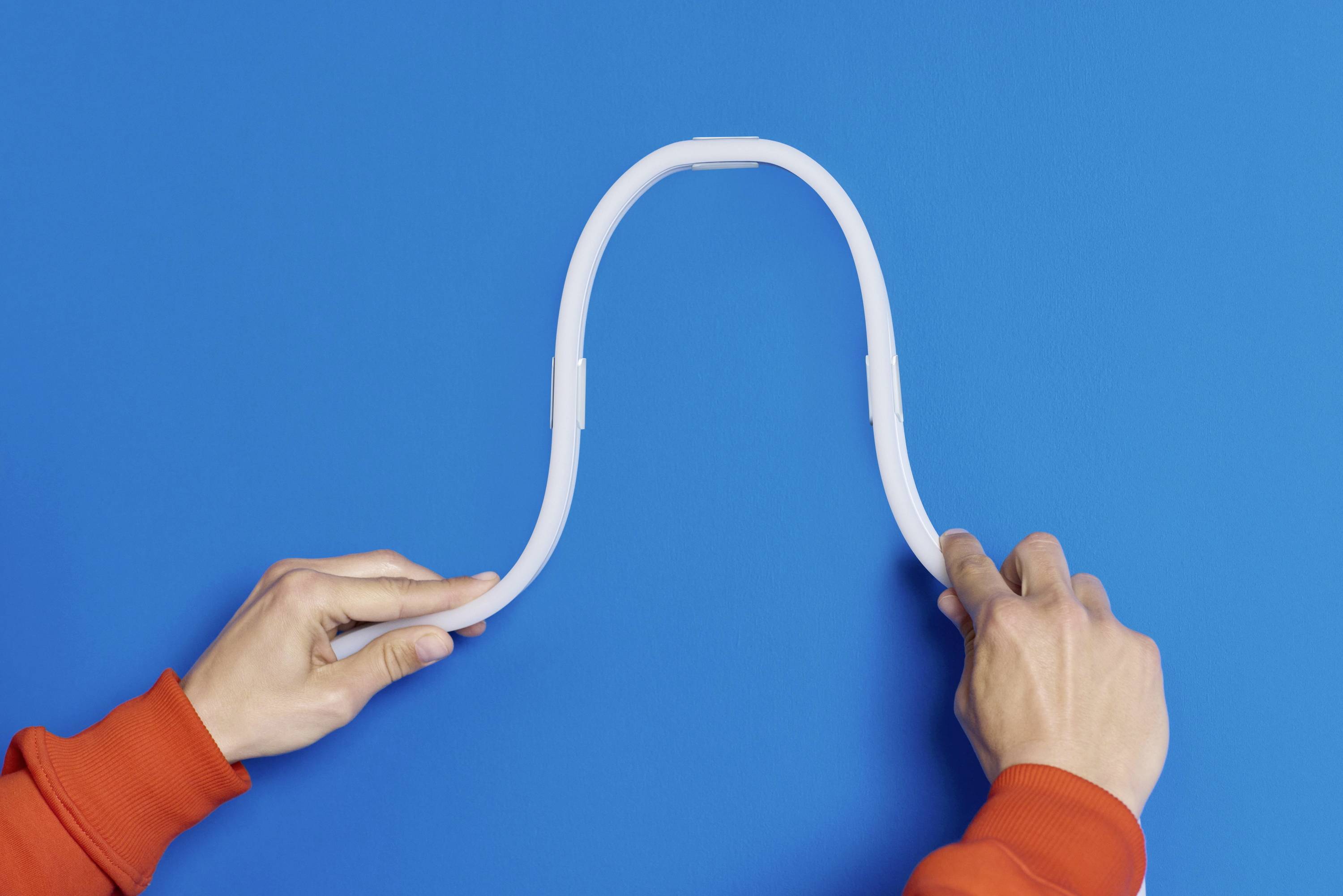 Zwei Hände in roten Ärmeln biegen ein weißes, flexibles Rohr in Form eines umgekehrten 'U' vor blauem Hintergrund.