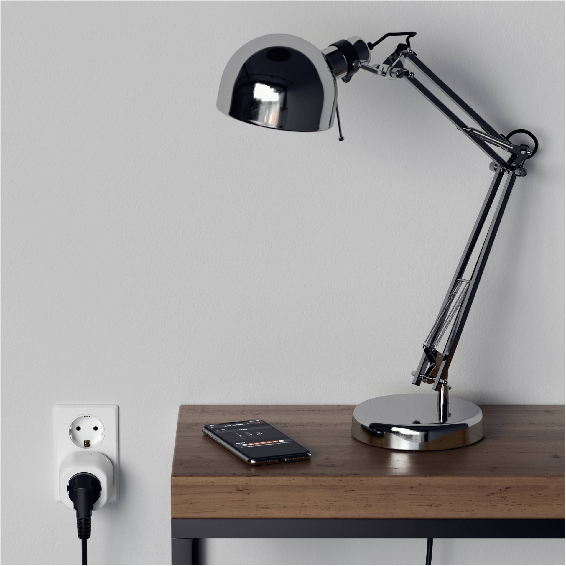 Eine Schreibtischlampe aus Metall beleuchtet einen Holztisch, auf dem ein Smartphone liegt. Rechts von der Lampe führt ein eingestecktes Kabel in eine Steckdose.