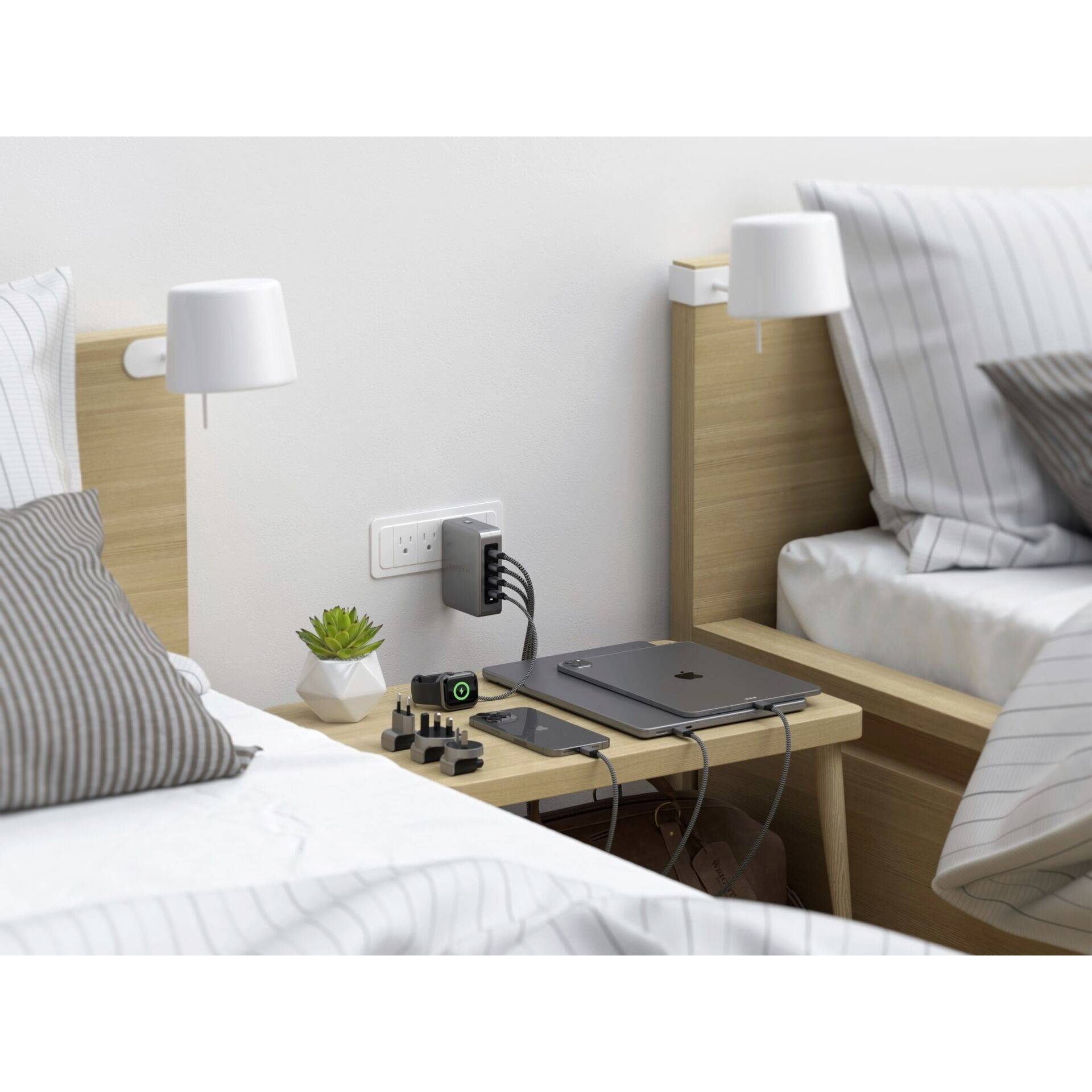 Zwei Betten mit Holzkopfteil, dazwischen ein kleiner Tisch mit Laptop, Tablet, Steckdosenadapter und Ladekabeln.