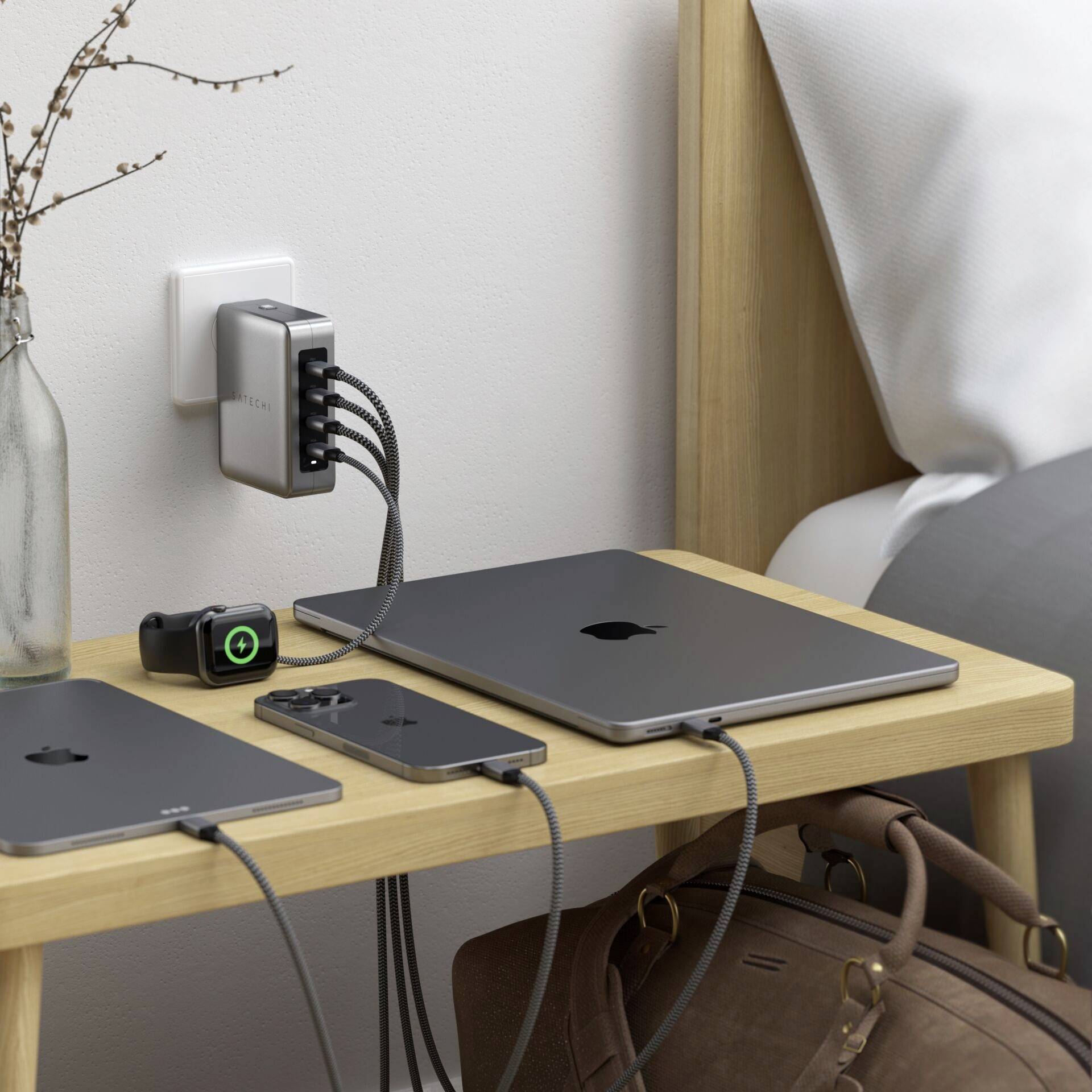 'Ein Nachttisch mit einem Laptop, Smartphone und Tablet, die an einen Mehrfachstecker angeschlossen sind, der an der Wandmontage befestigt ist.'