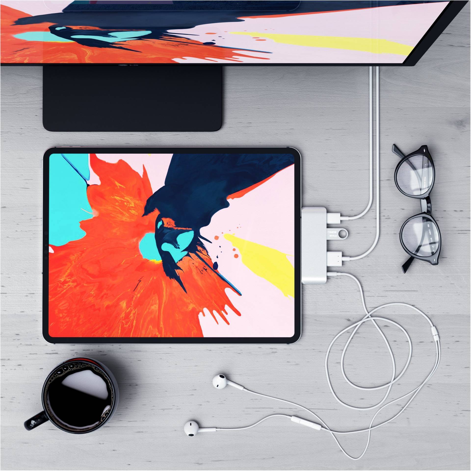 Ein Tablet mit farbenfroher digitaler Kunst auf einem Tisch, daneben eine Brille, ein Smartphone, Kopfhörer und eine Kaffeetasse.