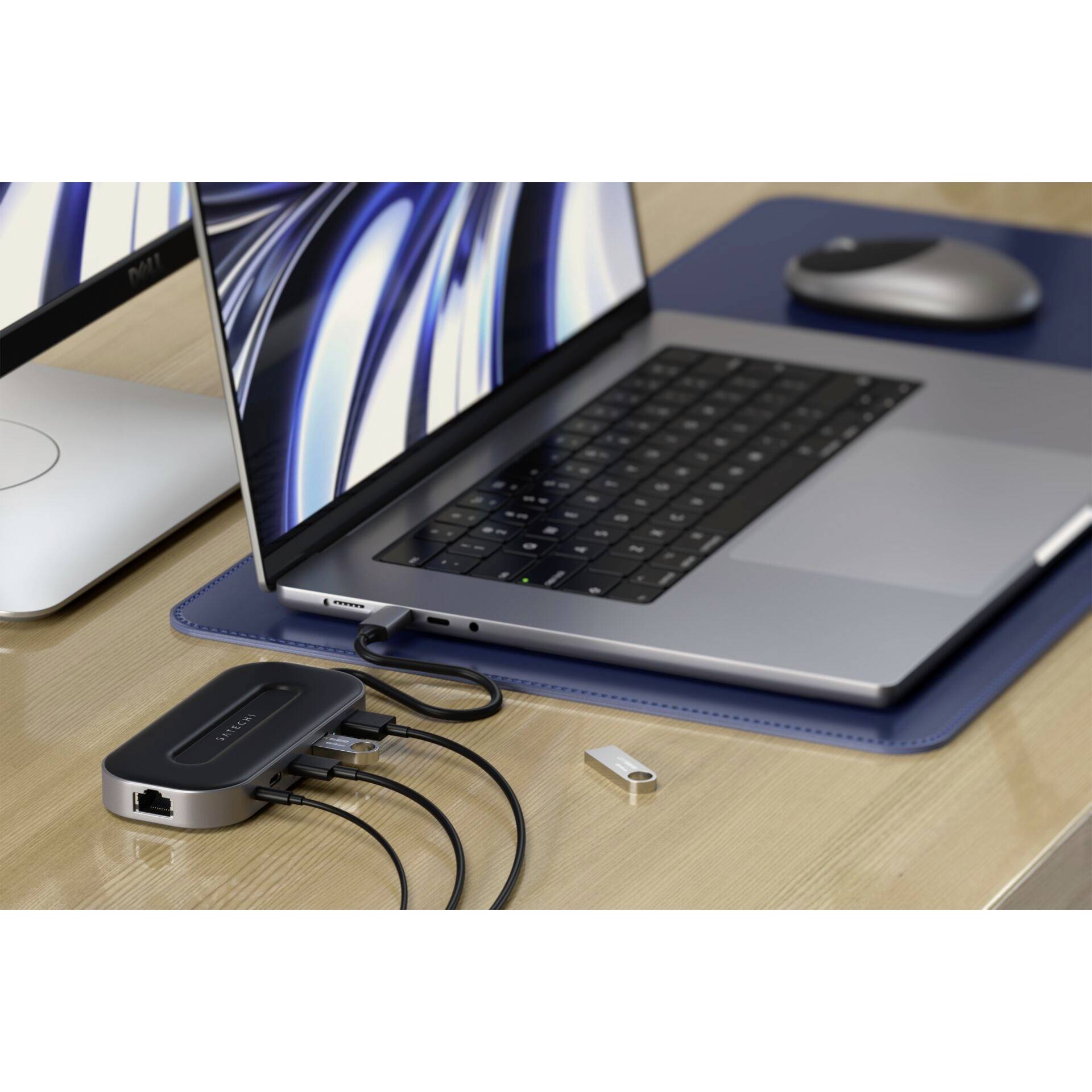 Ein Laptop mit angeschlossenem USB-Hub liegt auf einem Schreibtisch. Mehrere Kabel sind an den Hub angeschlossen. Ein Monitor und eine Maus sind daneben platziert.