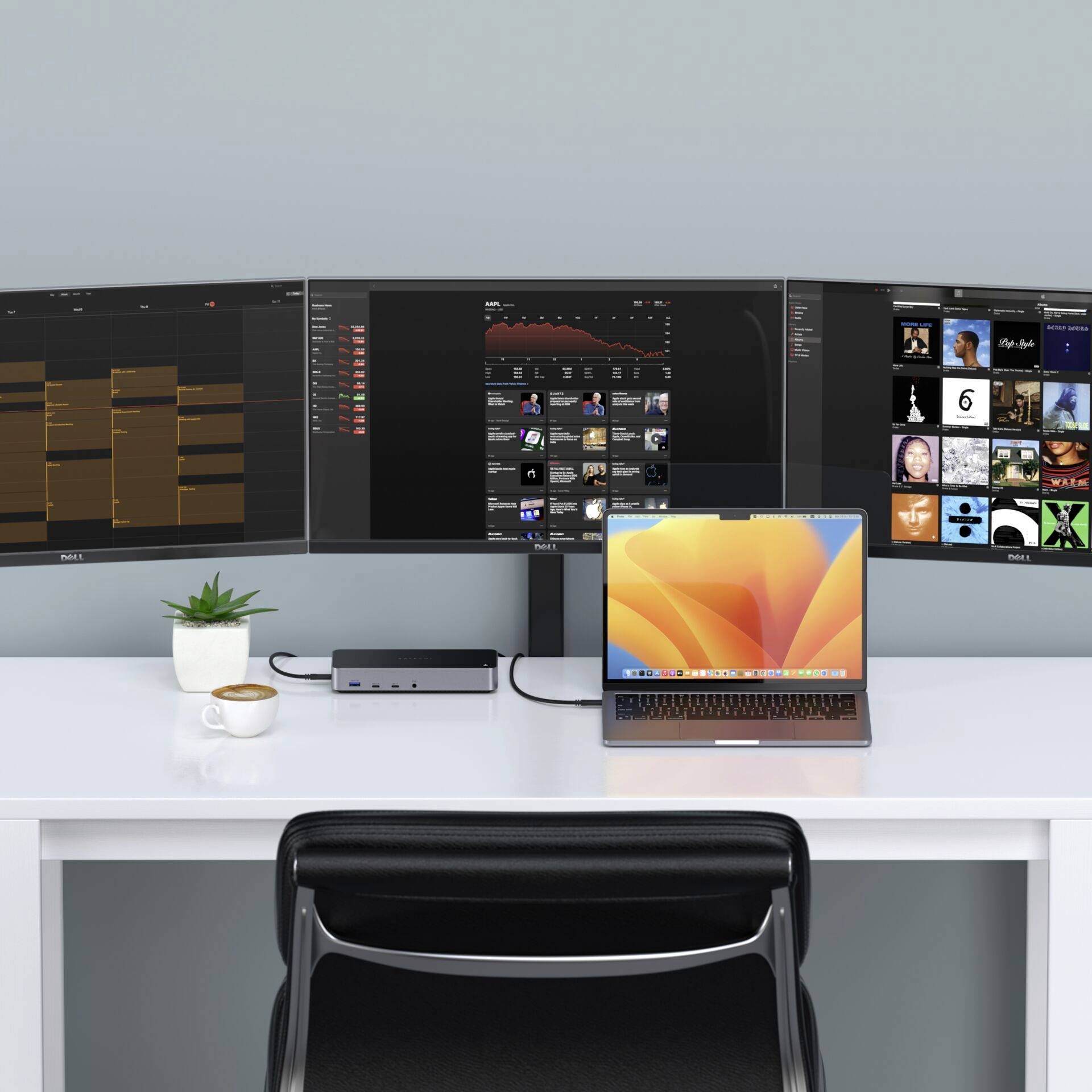 Ein Büroarbeitsplatz mit einem Laptop, eingesteckt in mehrere Monitore, einer Pflanze und einer Tasse auf einem weißen Schreibtisch.