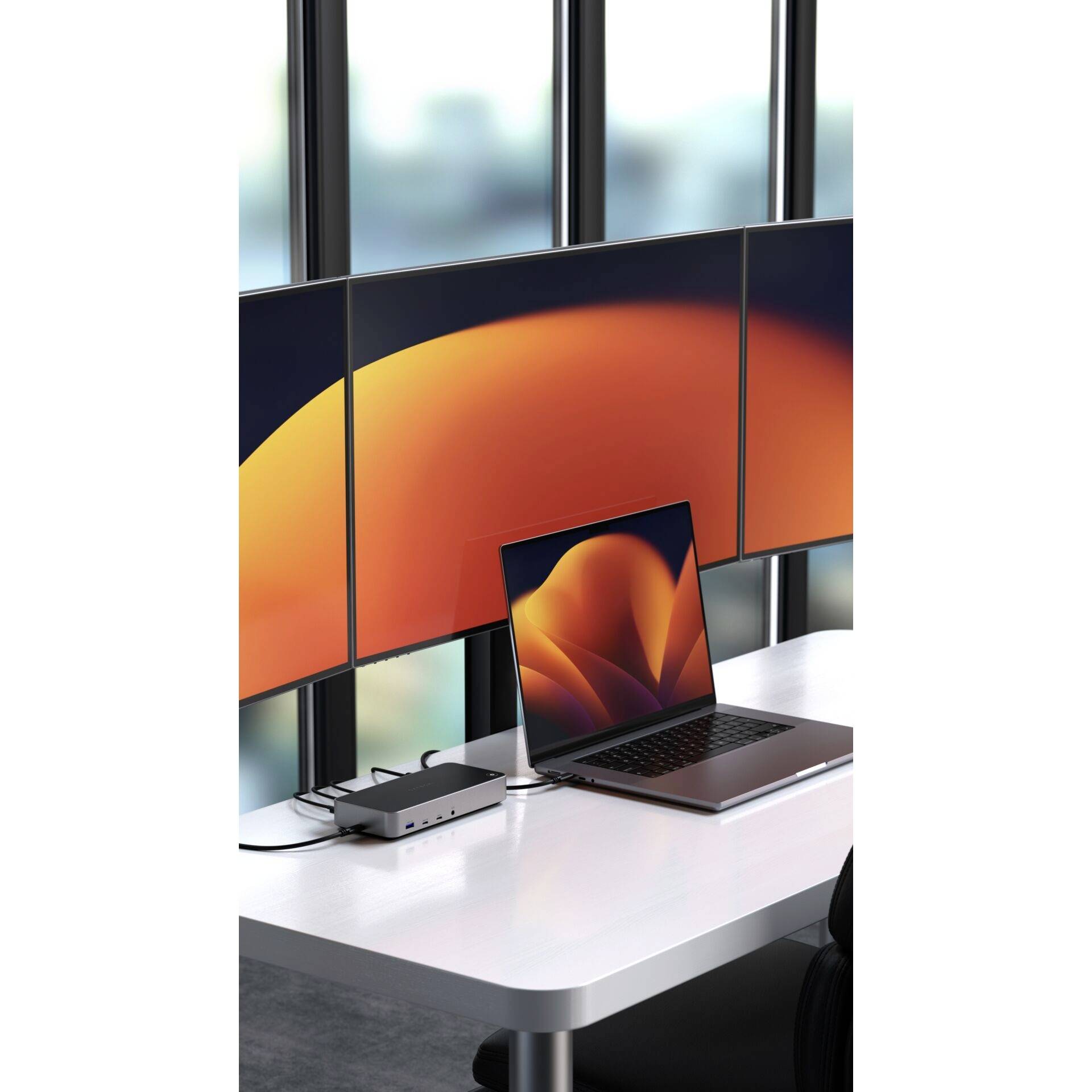 Ein Laptop auf einem Tisch ist an einen Dockingstation angeschlossen und steuert vier große Monitore mit leuchtend warmem Bildschirmhintergrund.