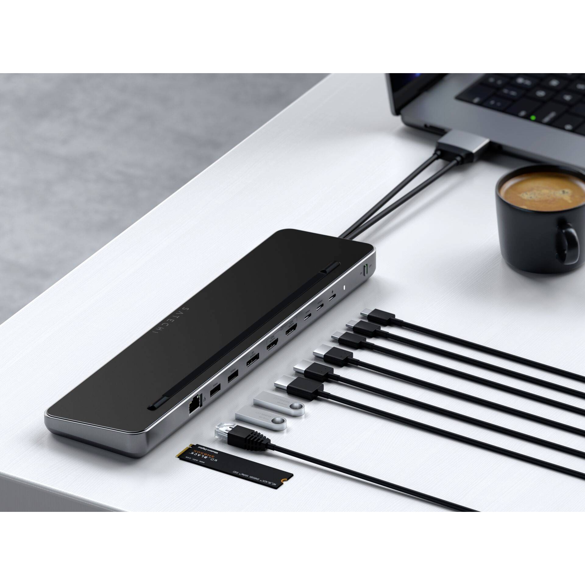 'USB-C-Dockingstation mit mehreren Anschlüssen und Kabeln auf einem Schreibtisch, mit einem Laptop verbunden. Daneben steht eine Tasse Kaffee.'