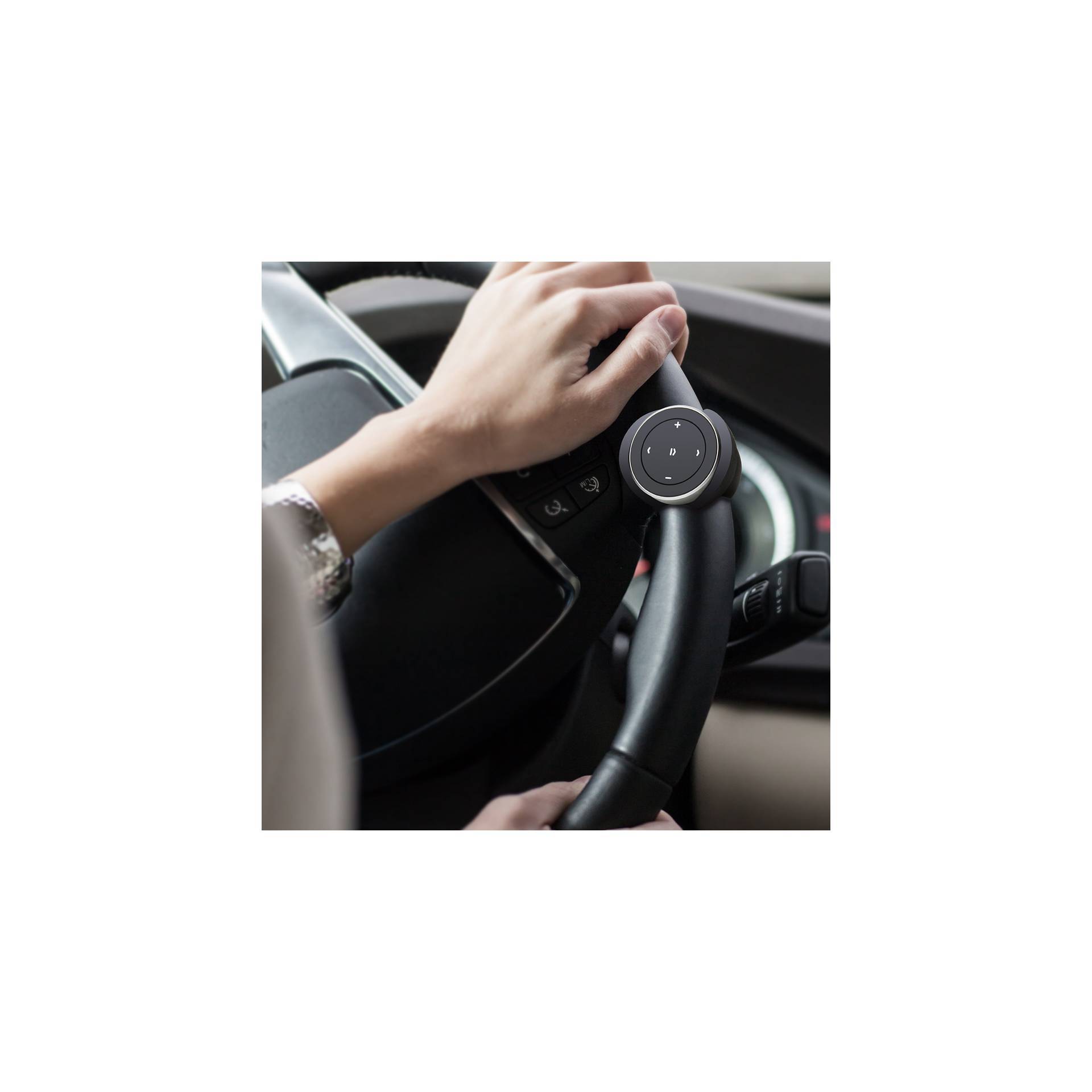 Eine Hand auf einem Lenkrad, die ein kleines rundes Gerät mit Knöpfen hält, vermutlich zur Steuerung von Funktionen im Auto.