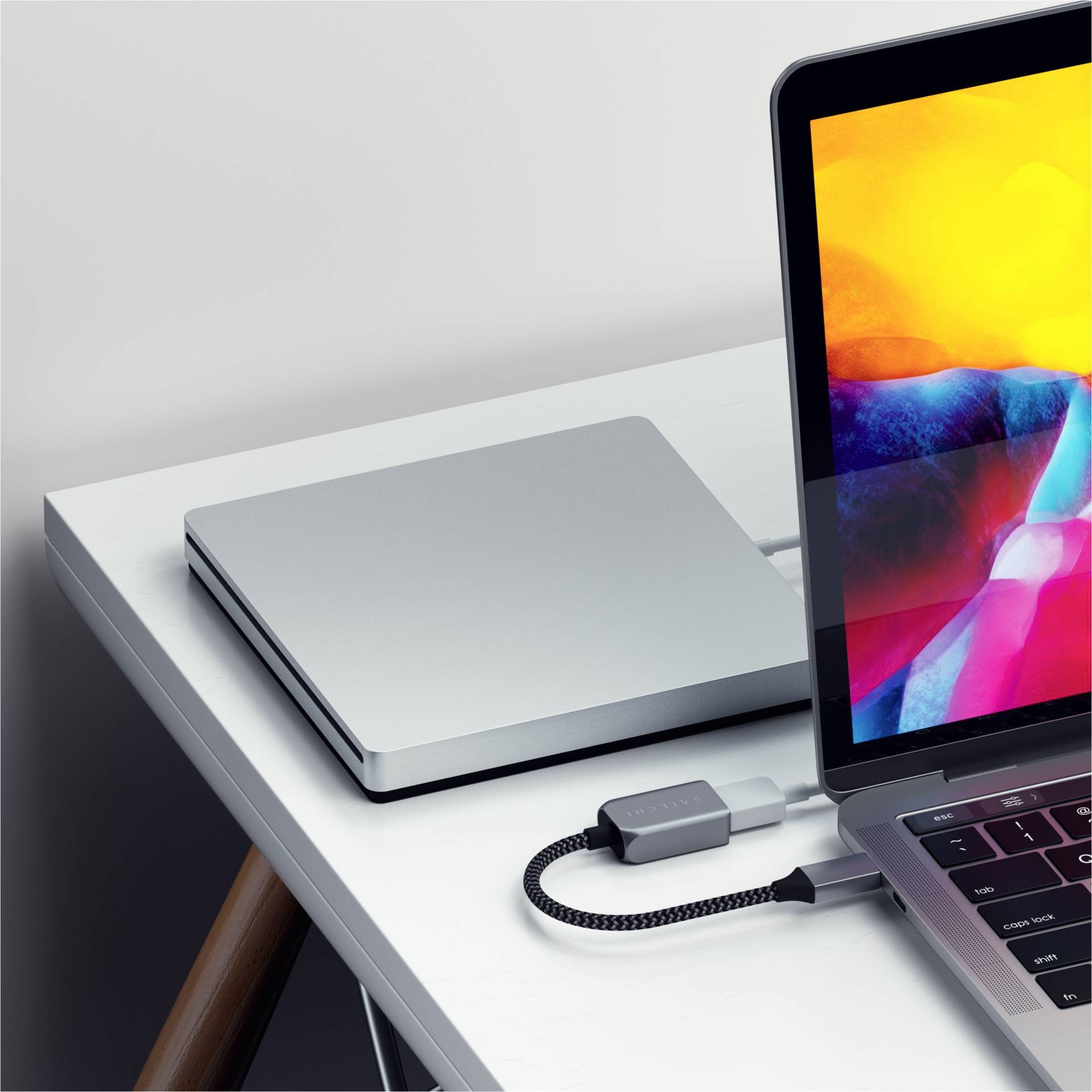 Laptop auf einem Tisch, angeschlossen an eine externe Festplatte. Der Bildschirm zeigt bunte Grafiken. Im Hintergrund liegt ein geschlossenes Laptop.