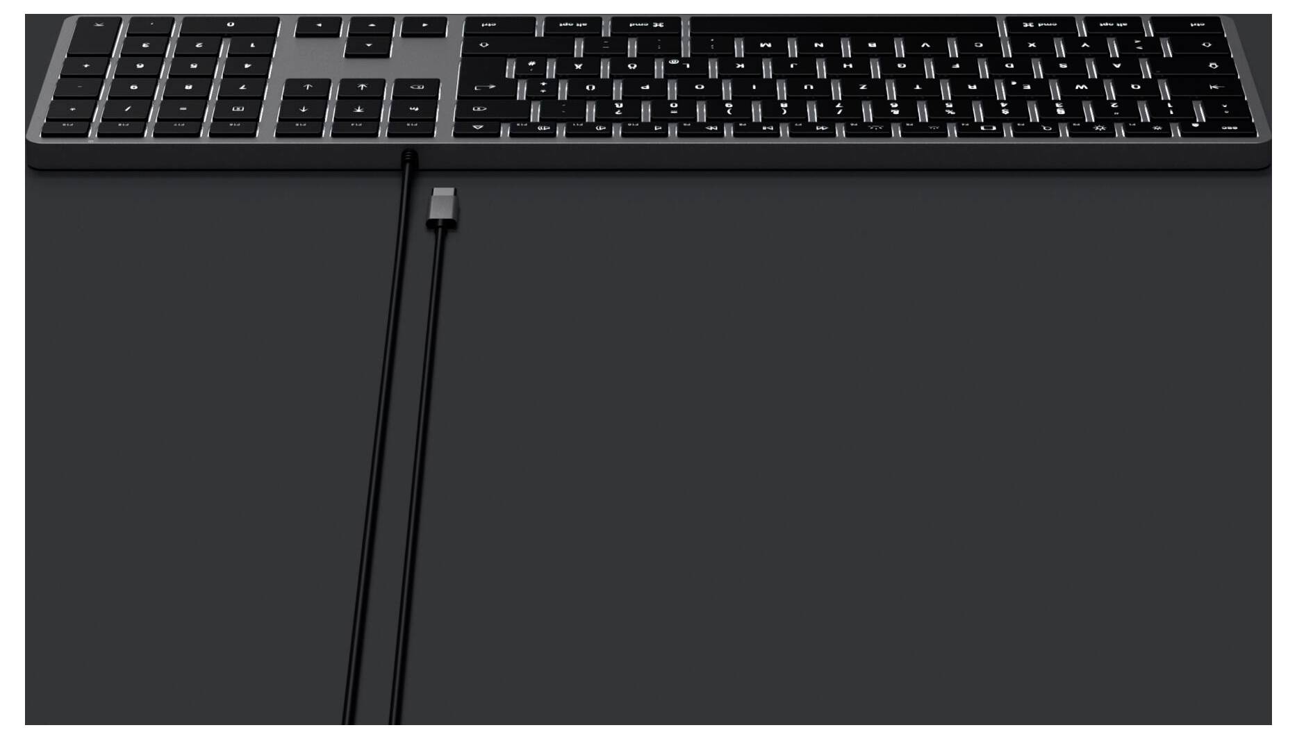 Eine schwarze Tastatur liegt auf einem dunklen Tisch, daneben verläuft ein schwarzes Kabel nach unten.