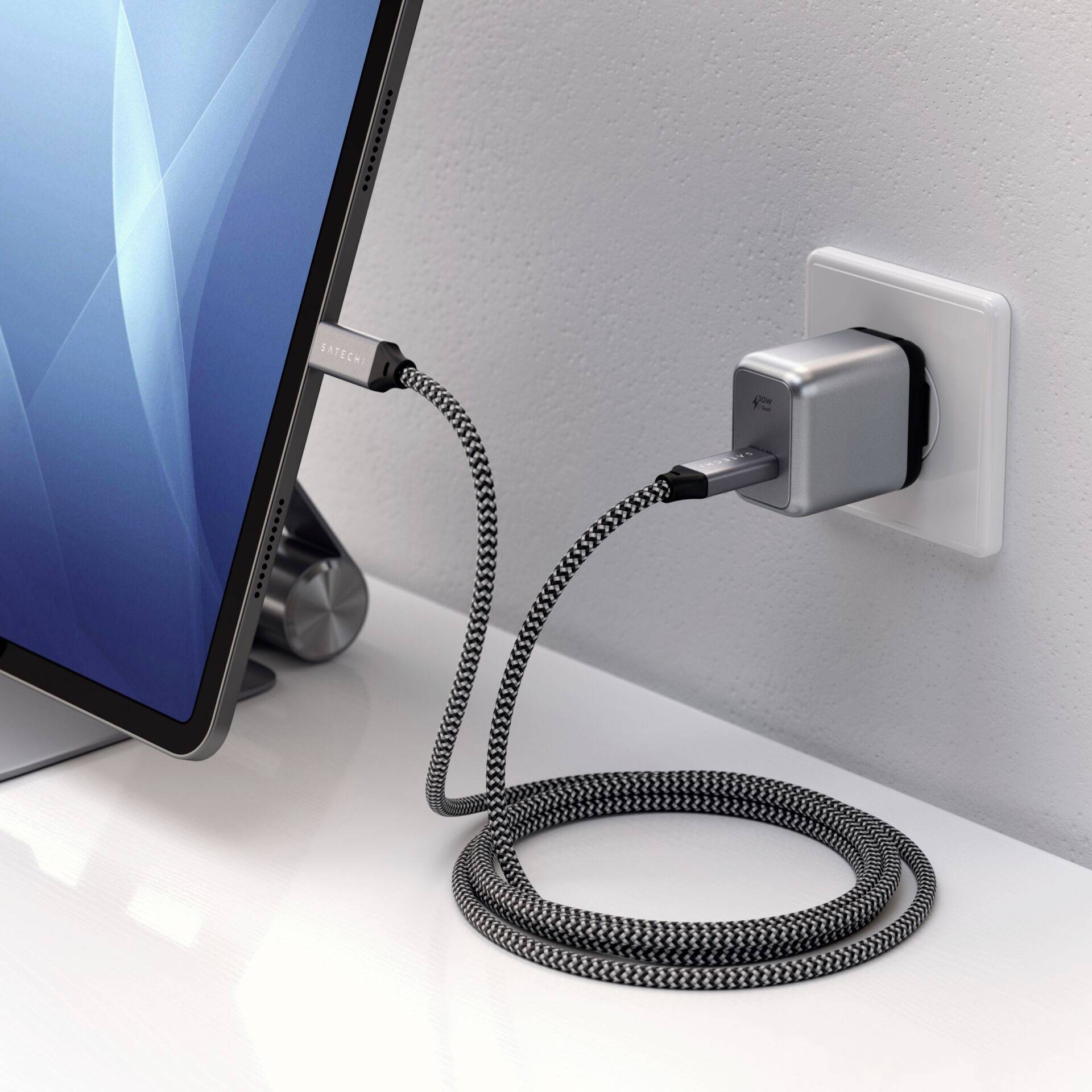 Ein Tablet ist mit einem gewebten Ladekabel an eine Steckdose angeschlossen. Das Gerät wird auf einem weißen Tisch geladen.