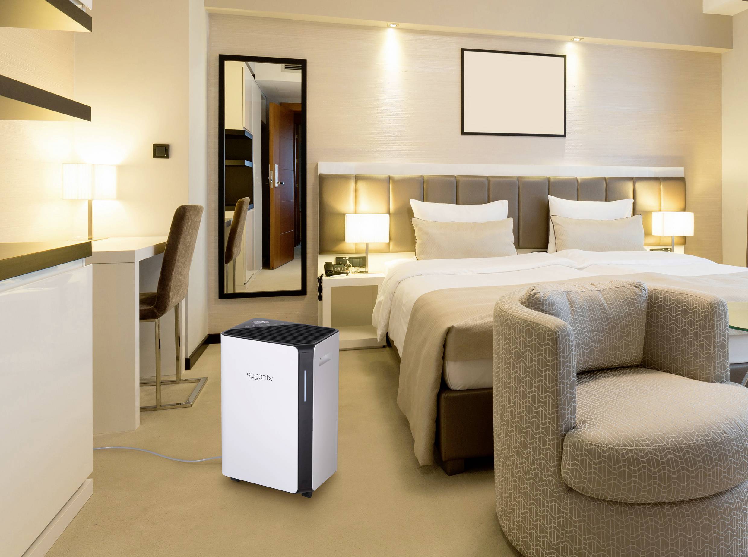 Ein modernes Hotelzimmer mit einem Doppelbett, Schreibtisch und Sessel. Ein Luftreiniger steht auf dem Boden nahe dem Bett.