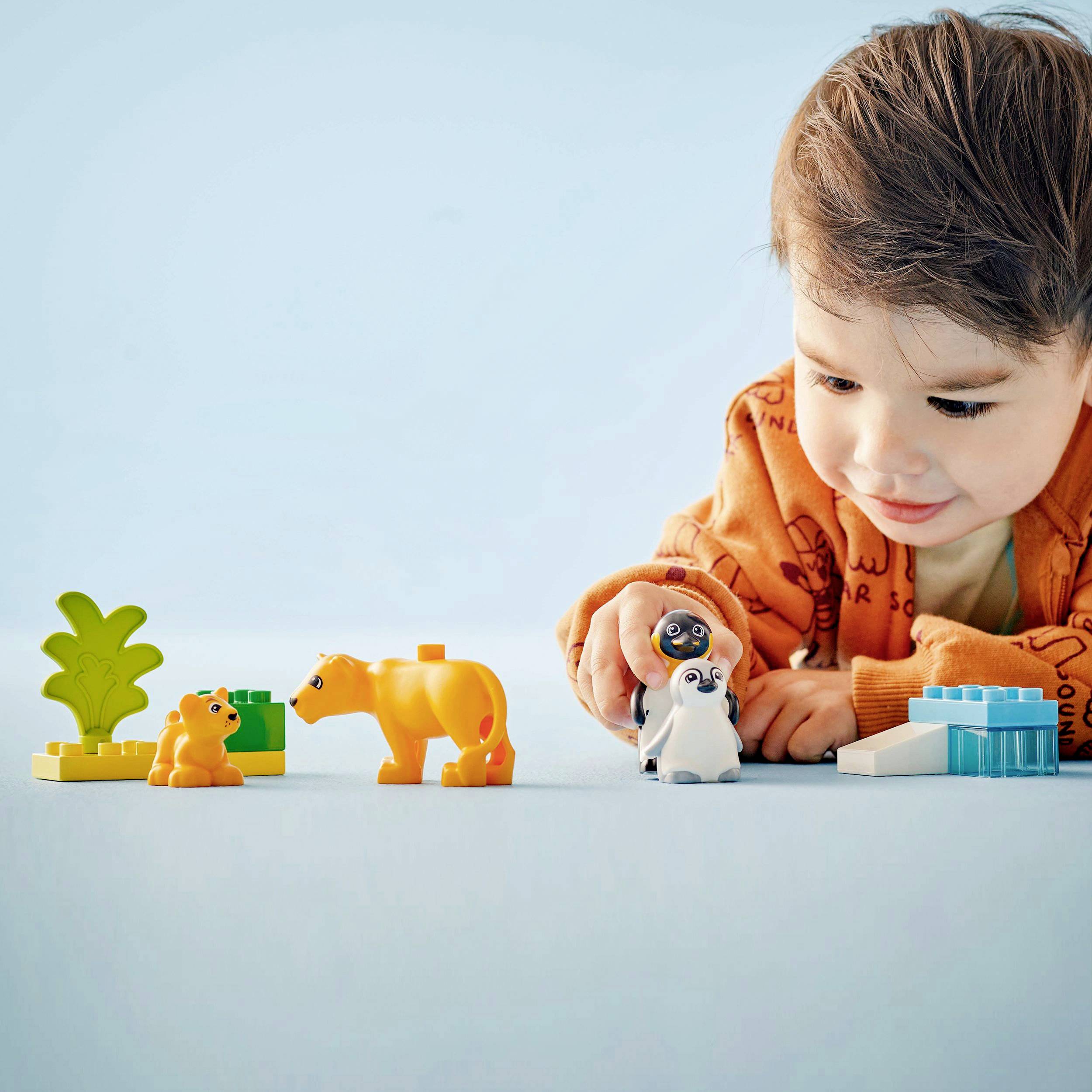 Ein Kleinkind sitzt auf dem Boden und spielt mit bunten Bausteinen und Tierfiguren. Der Hintergrund ist hellblau.