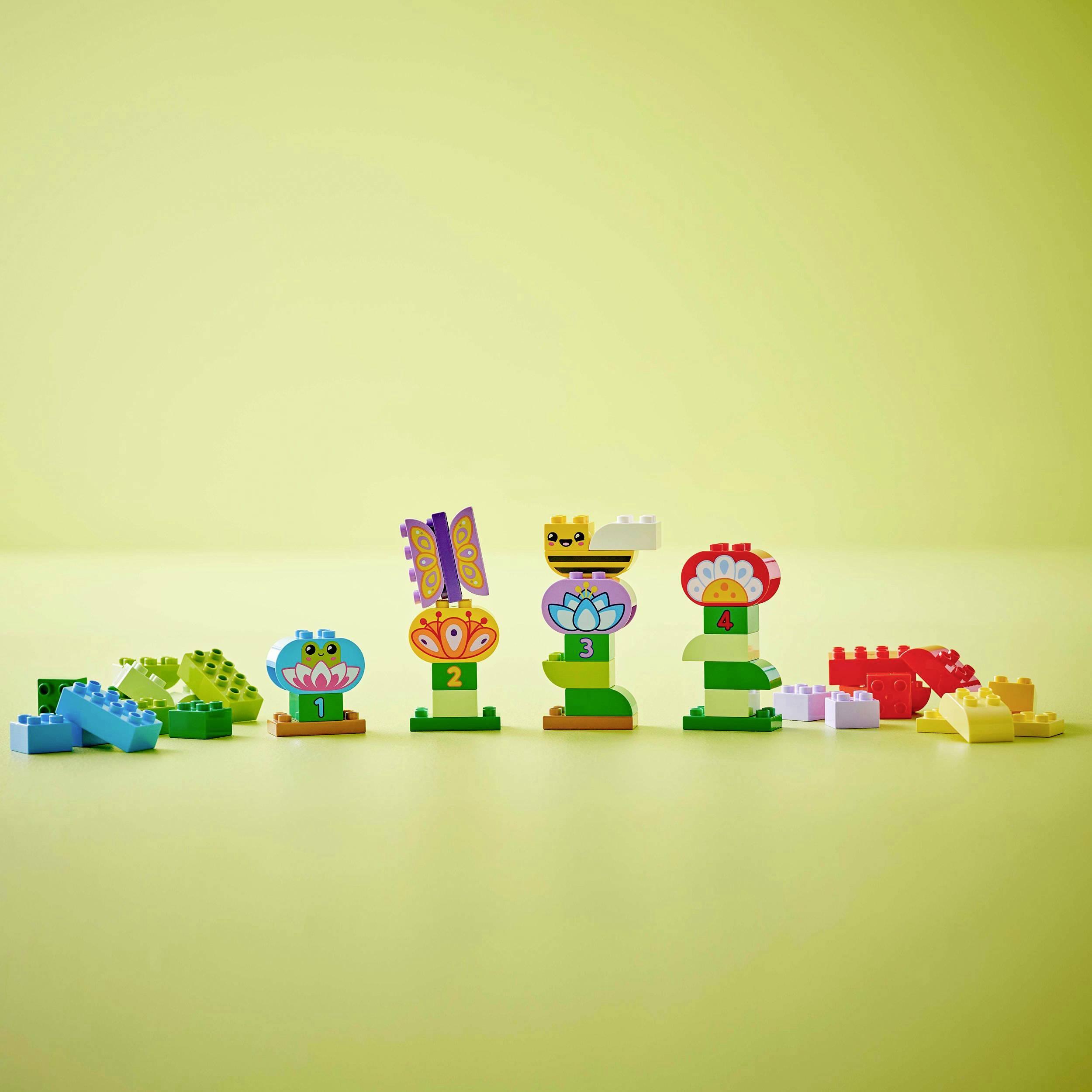 Bunte LEGO-Steine in Form von Blumen mit Nummern 1 bis 5 davor, auf einem grünen Hintergrund. Einige lose Steine liegen daneben.